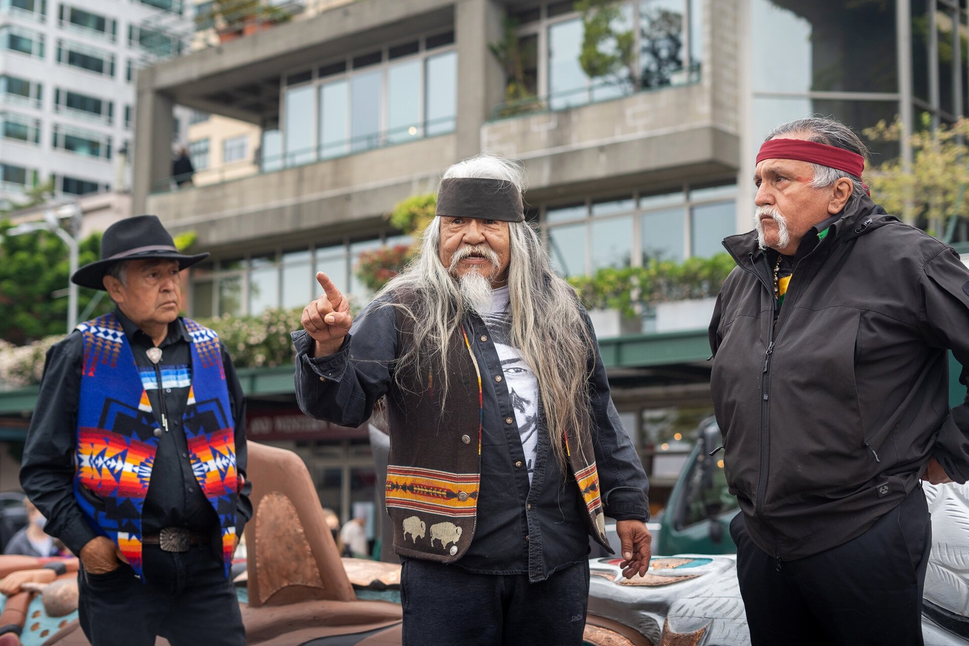  Master carvers from left, Douglas (Sit-ki-kadem) James, Rick Williams, and Jewell Praying Wolf James stand in front of the 24-foot totem pole while addressing the crowd on Saturday, May 22, 2021, outside of Seattle’s Pike Place Market. 