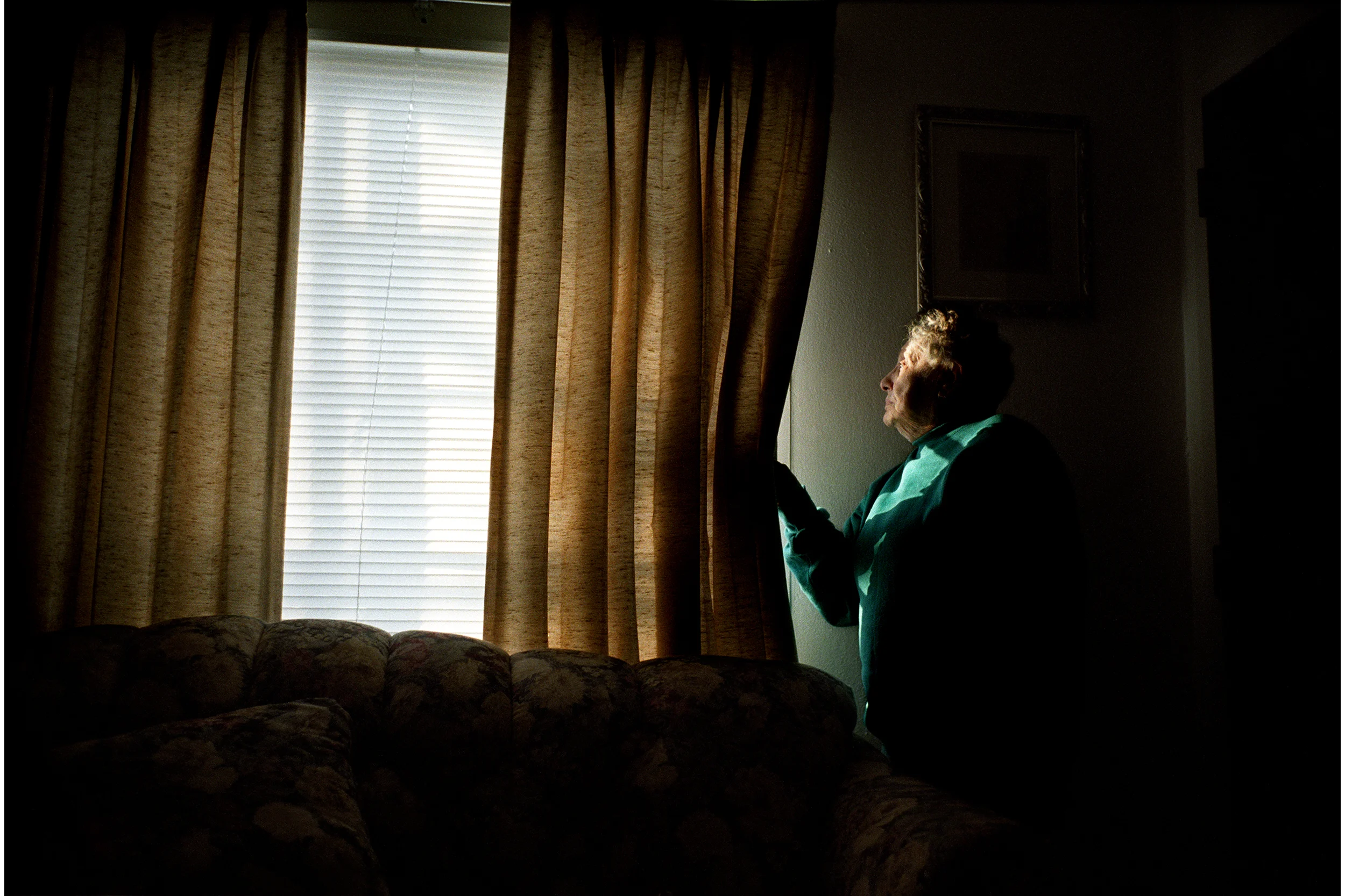 Eldery Woman Pulls Back Curtains to Look Out Window