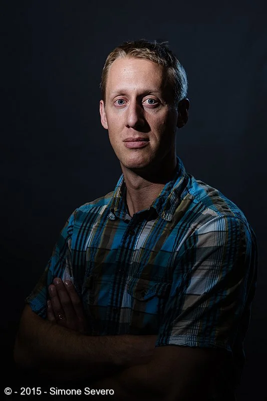 Sam was taking a workshop with me last night and agreed in being my portrait of the day when the class was over. I wanted a more harsh, dramatic look to this portrait so I used harsh light, a speedlight without any modifier pointing to his face and …