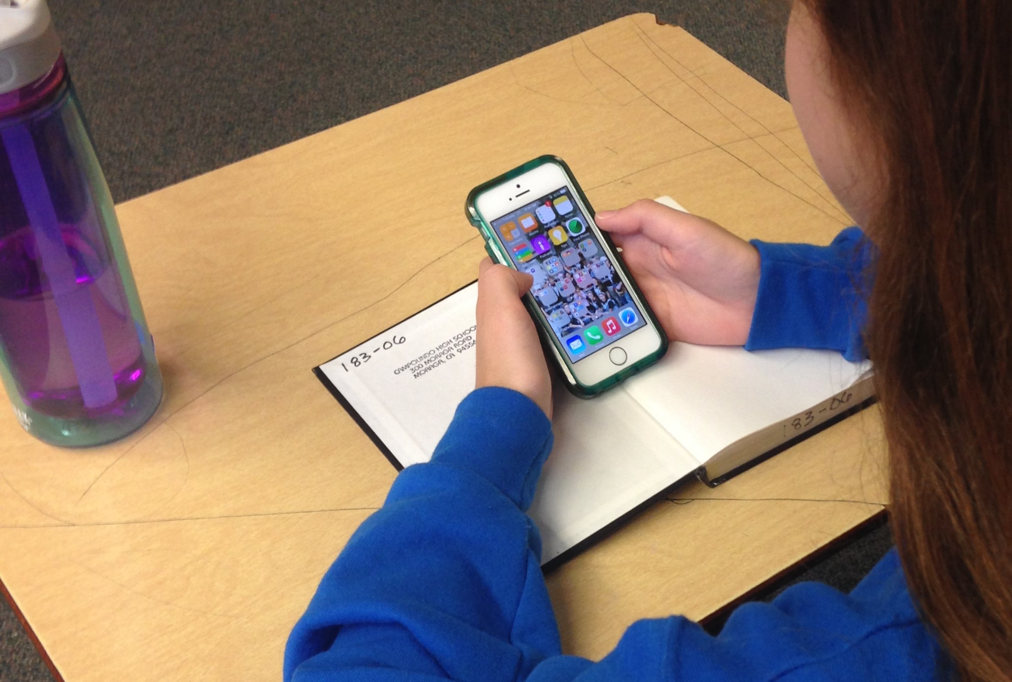 Niña distraída con un iPhone en el salón de clases