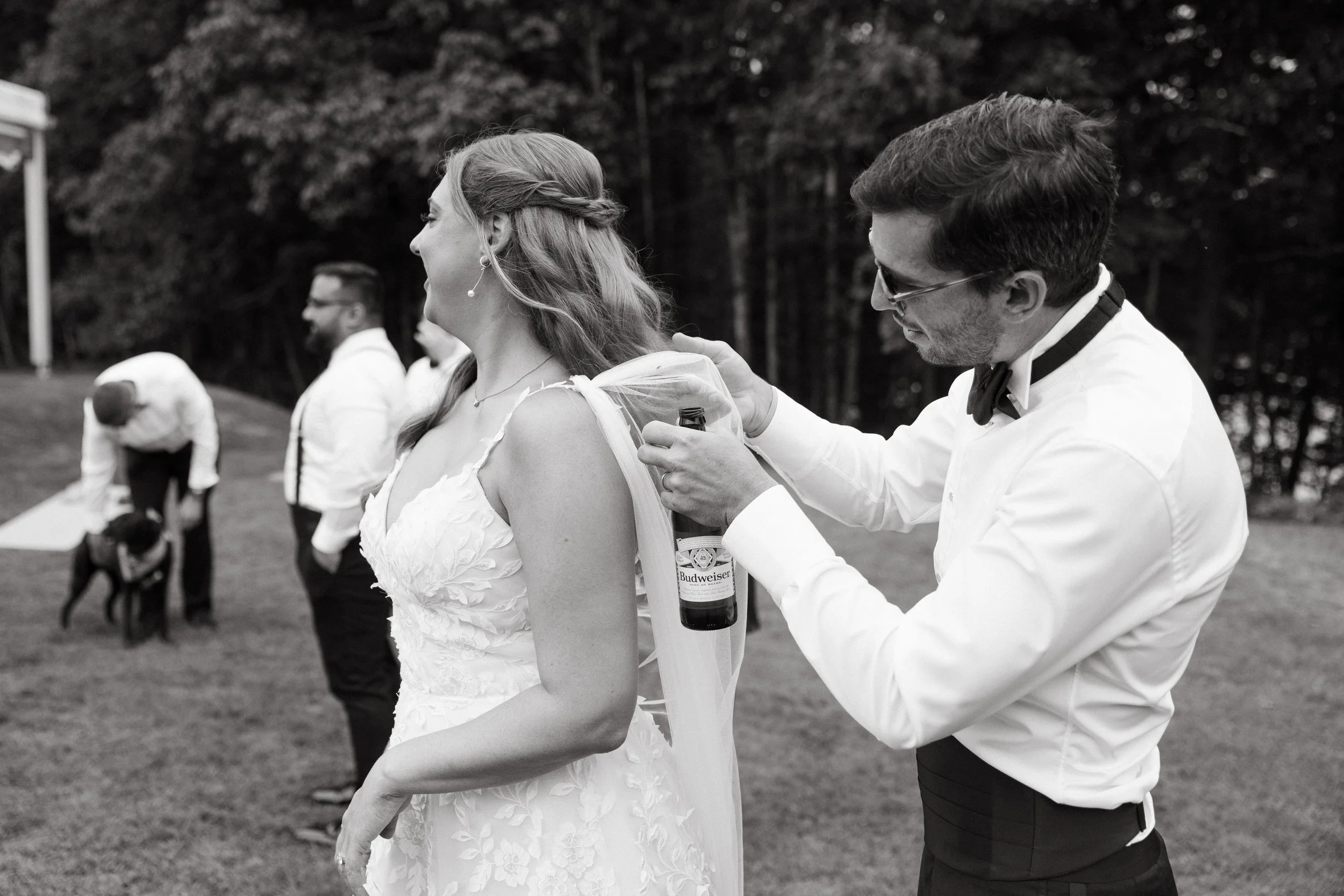 A friend helps the bride get a bug out of her dress during her wedding day at Marianmade Farm in Wiscasset, Maine. Photography by Sienna Renee Photography.