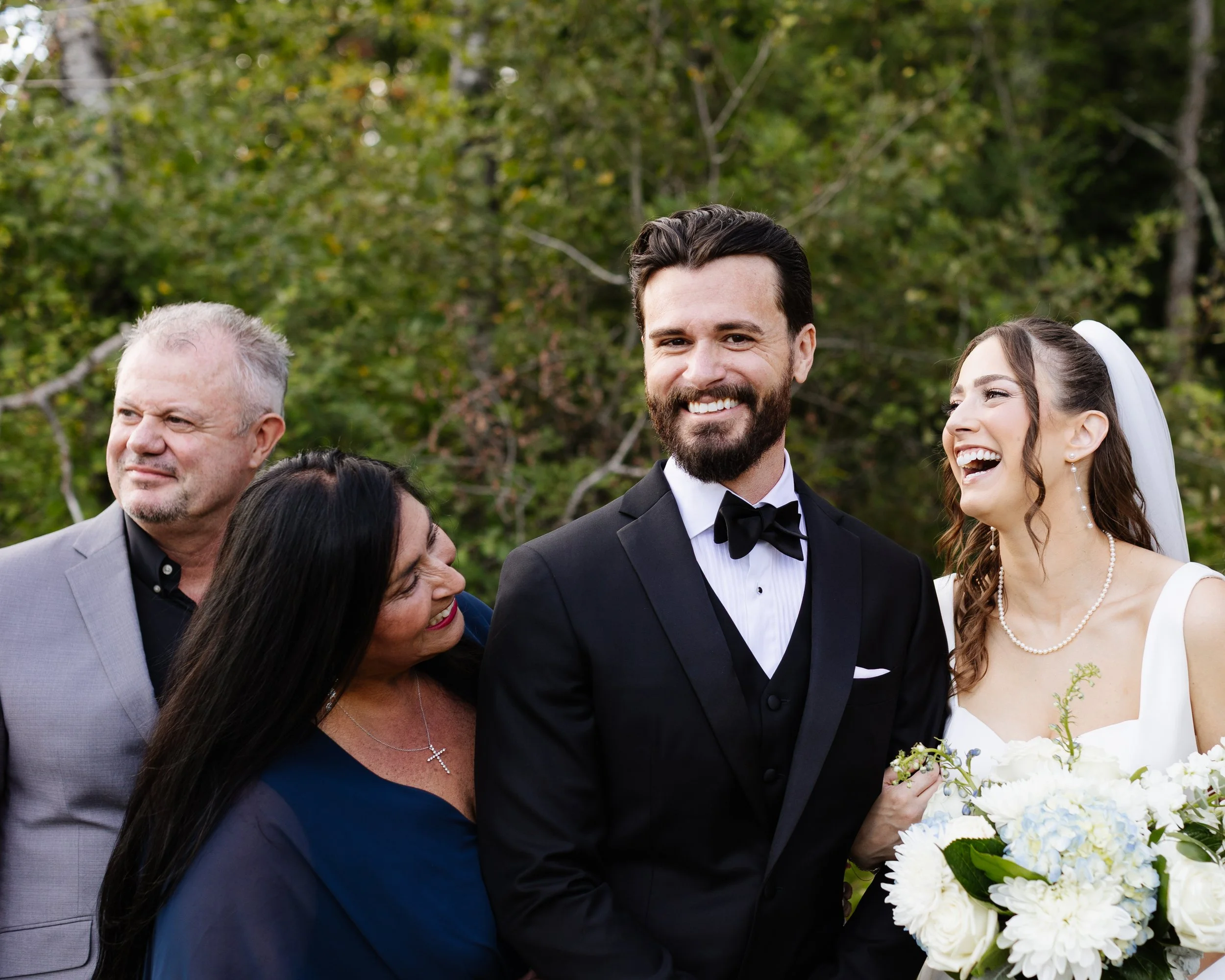 A couple laughing with their family during their small backyard wedding in Palmyra, Maine. Photography by Sienna Renee Photography.
