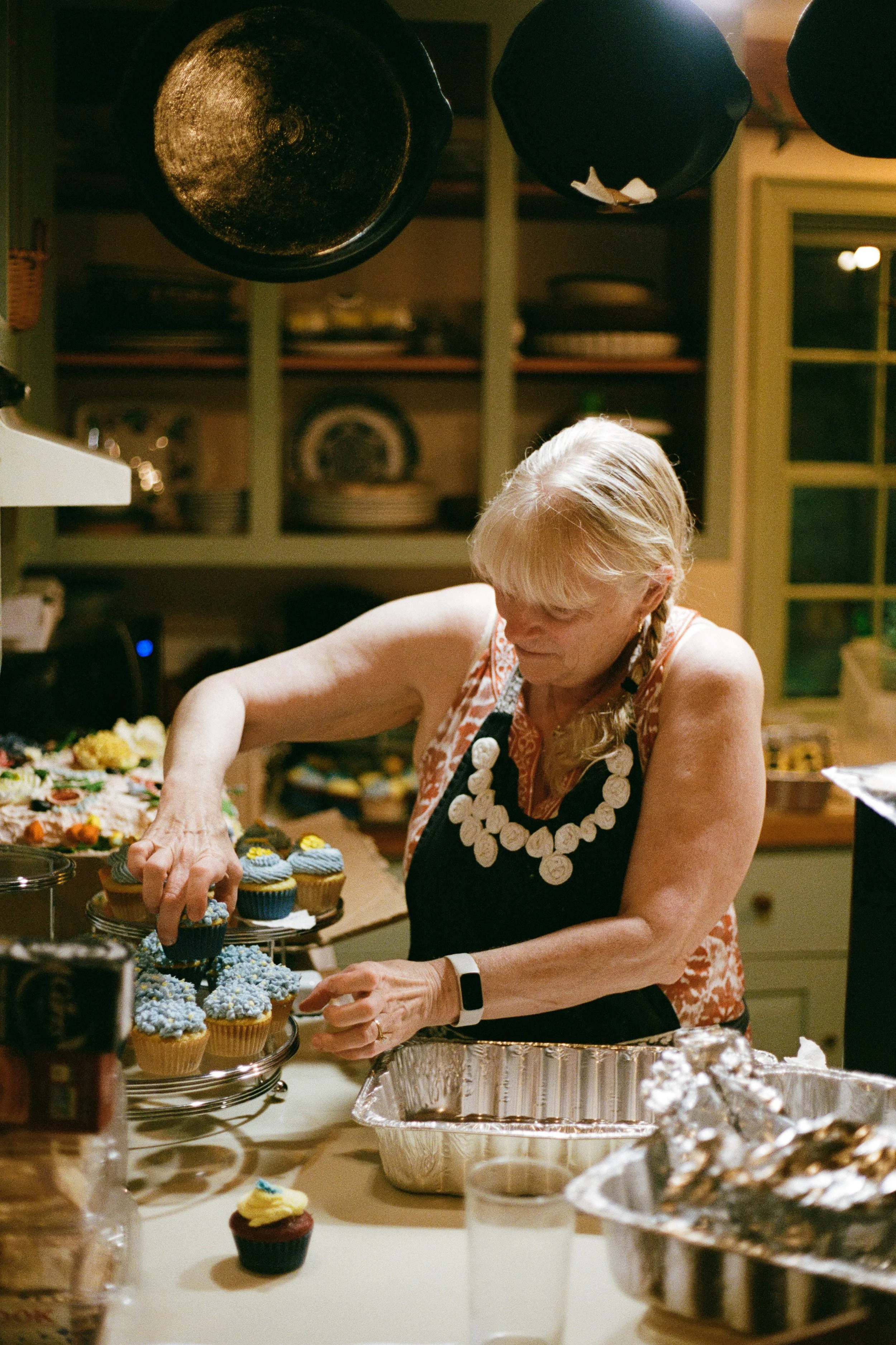 A family member places the cupcakes she made on a plate during a backyard wedding in North Berwick, Maine. Photography by Sienna Renee Photography.