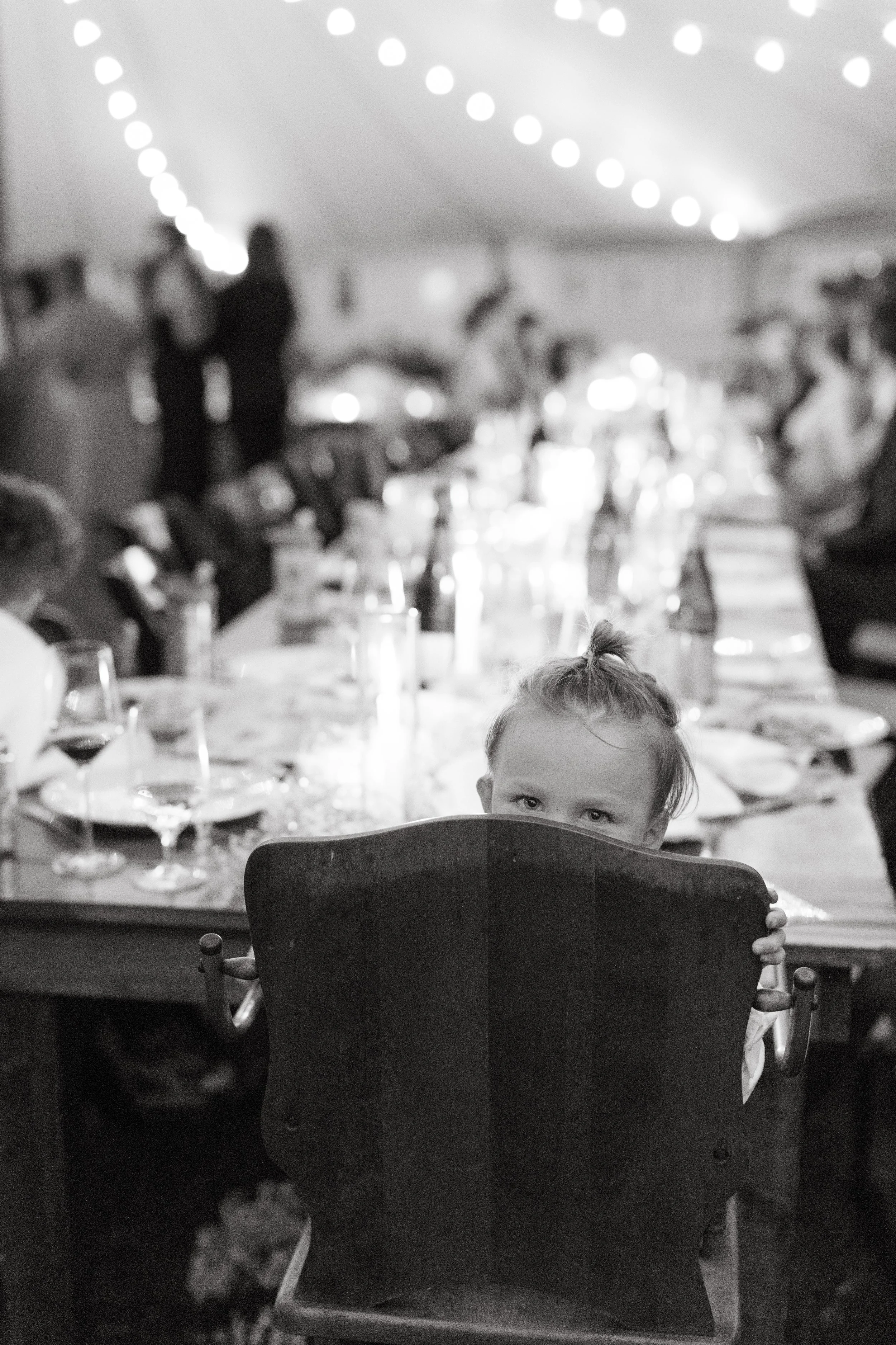 A child peeks over a chair during an intimate wedding in Kittery, Maine. Photography by Sienna Renee Photography.
