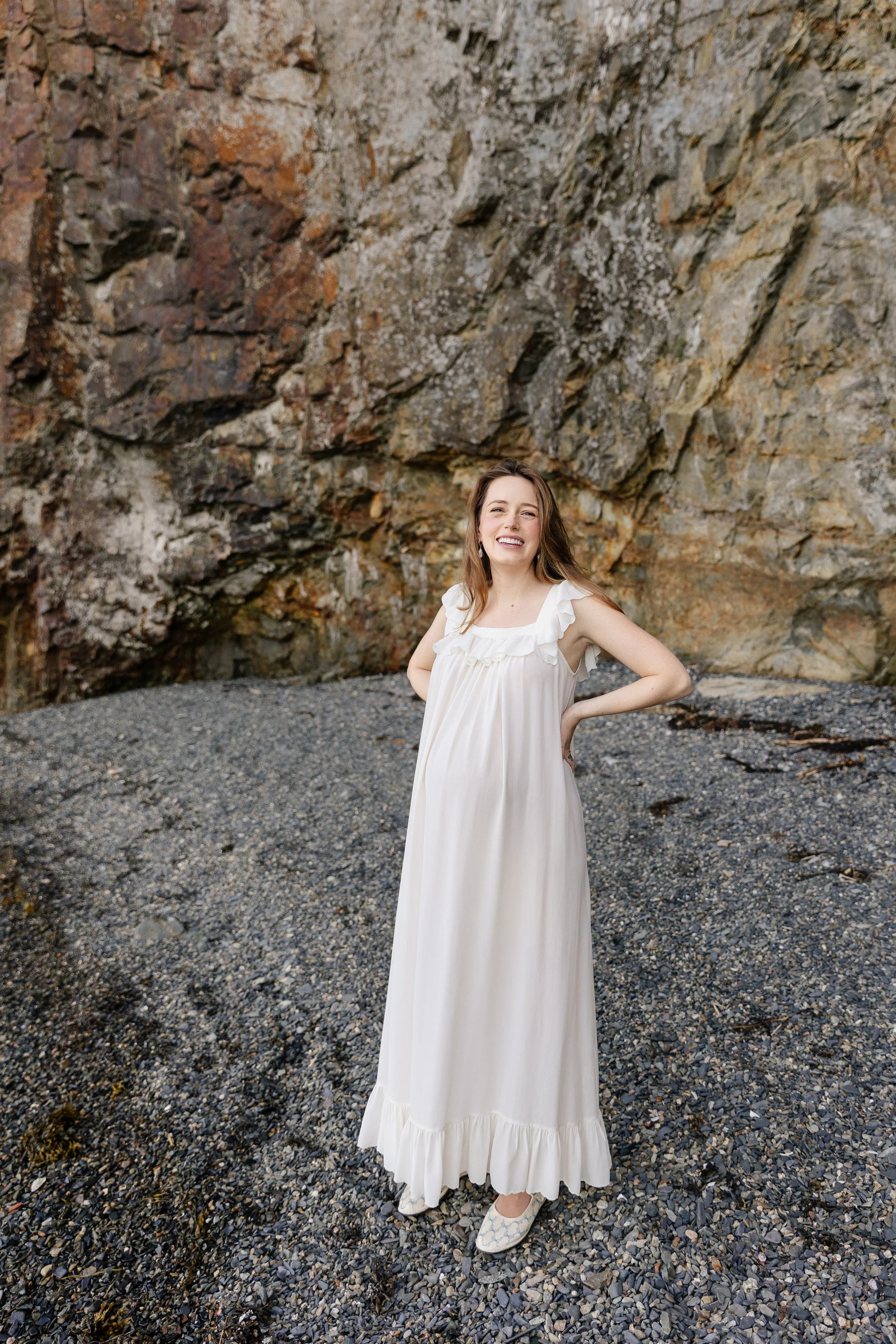An expecting mom stands on the beach during her babymoon in Bar Harbor, Maine. Photography by Sienna Renee Photography