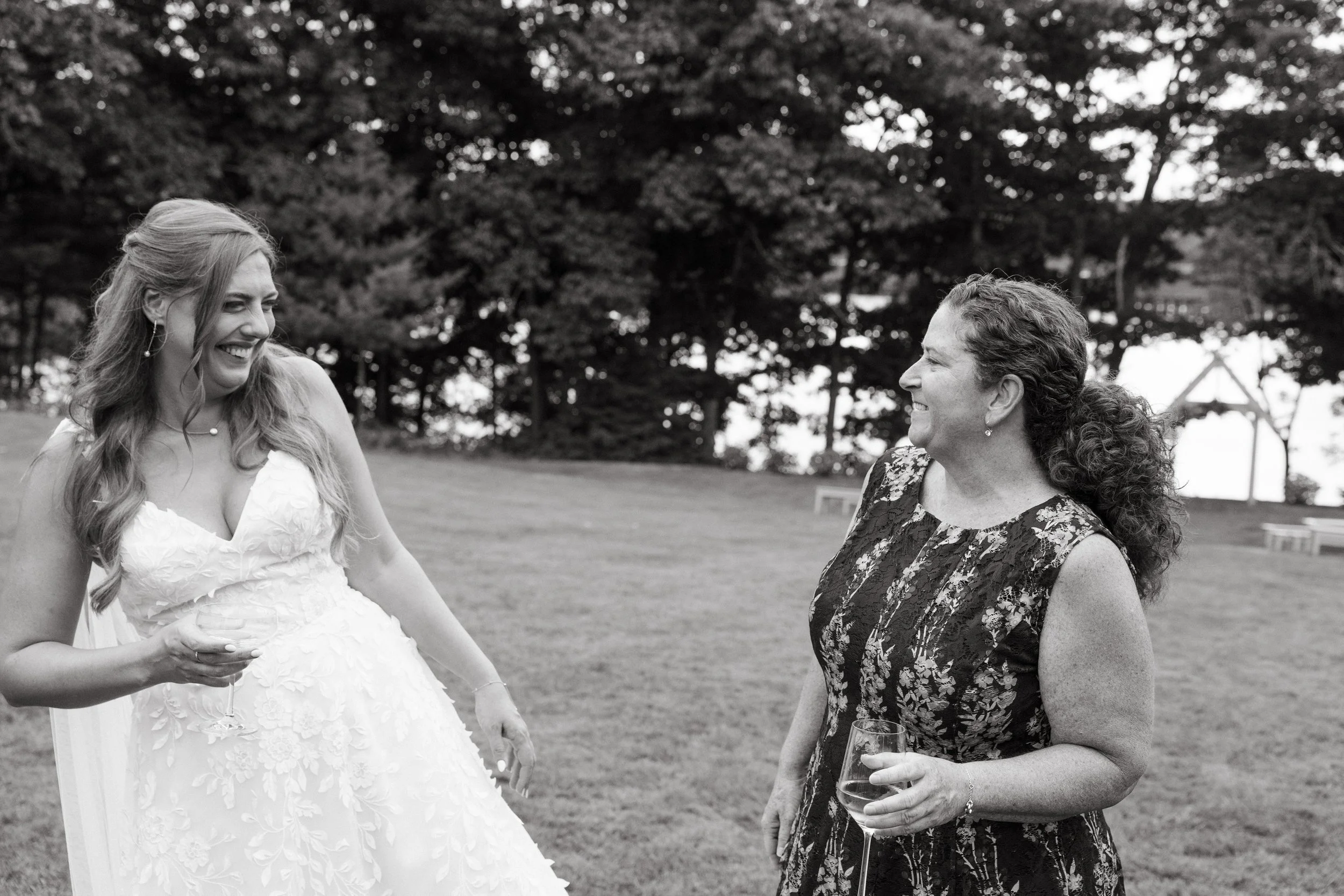 A bride and guest laugh as they chat during her wedding at Marianmade Farm in Wiscasset, Maine. Photography by Sienna Renee Photography.