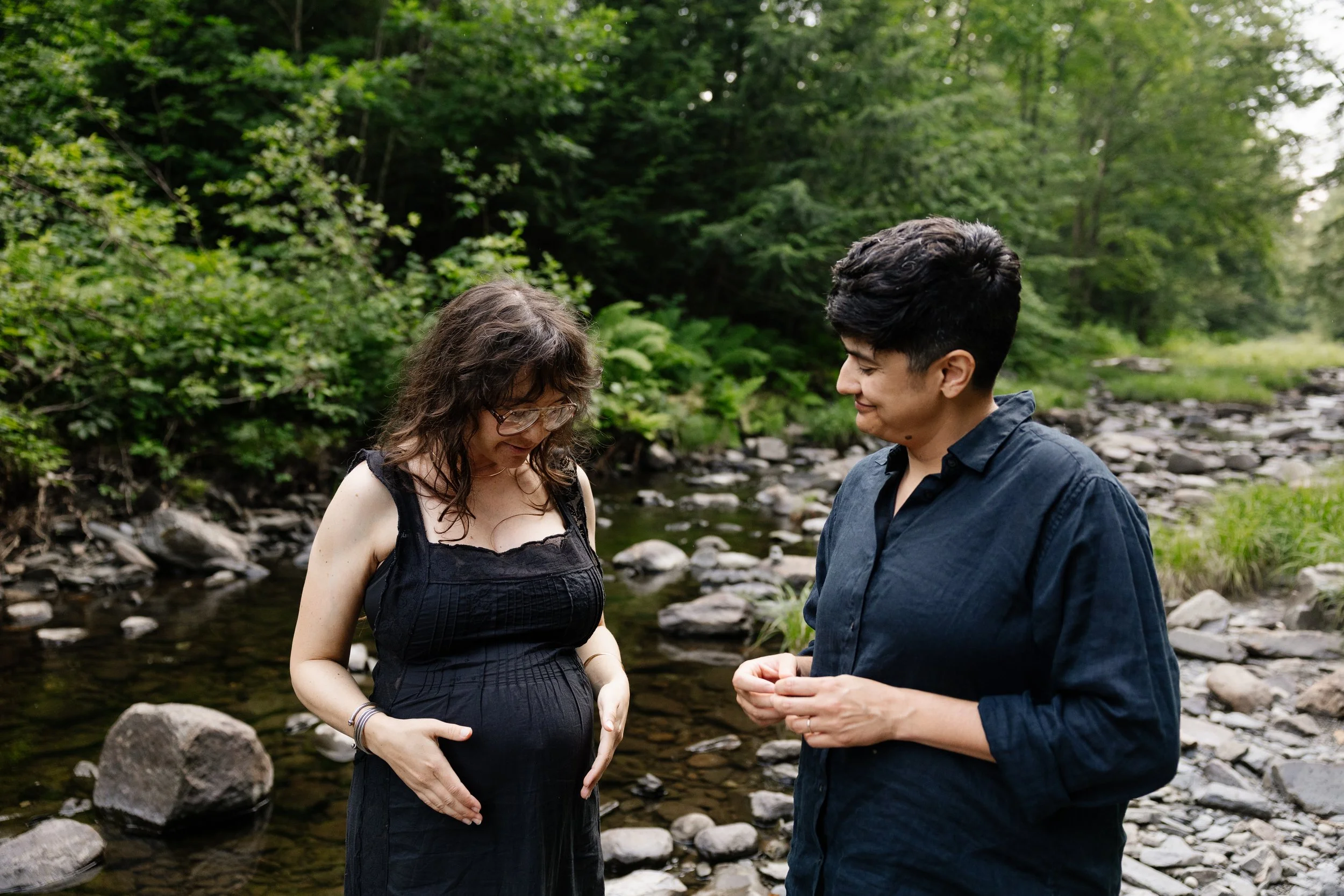 A couple smiles while talking about their pregnancy during a visit to Moosehead Lake, Maine. Photography by Sienna Renee Photography.
