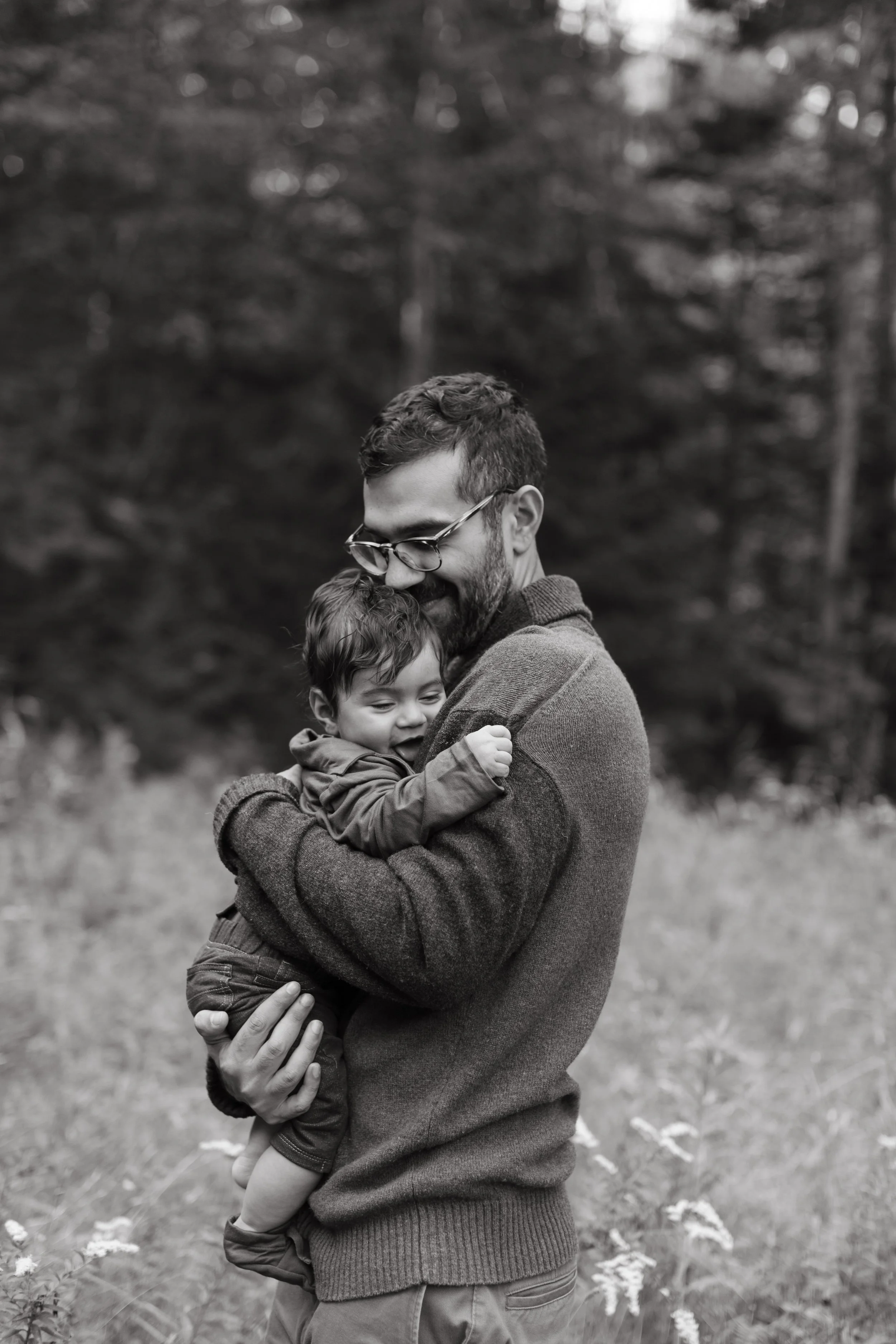 A father holds his baby close during a walk in the woods in Maine. Photography by Sienna Renee Photography.