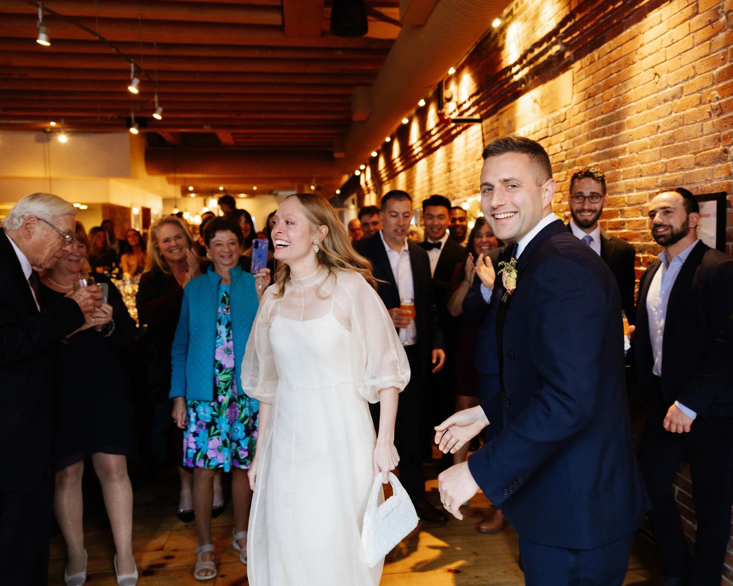 A couple smiles with guests during their wedding reception at Solo Italiano in Portland, Maine. Photography by Sienna Renee Photography.