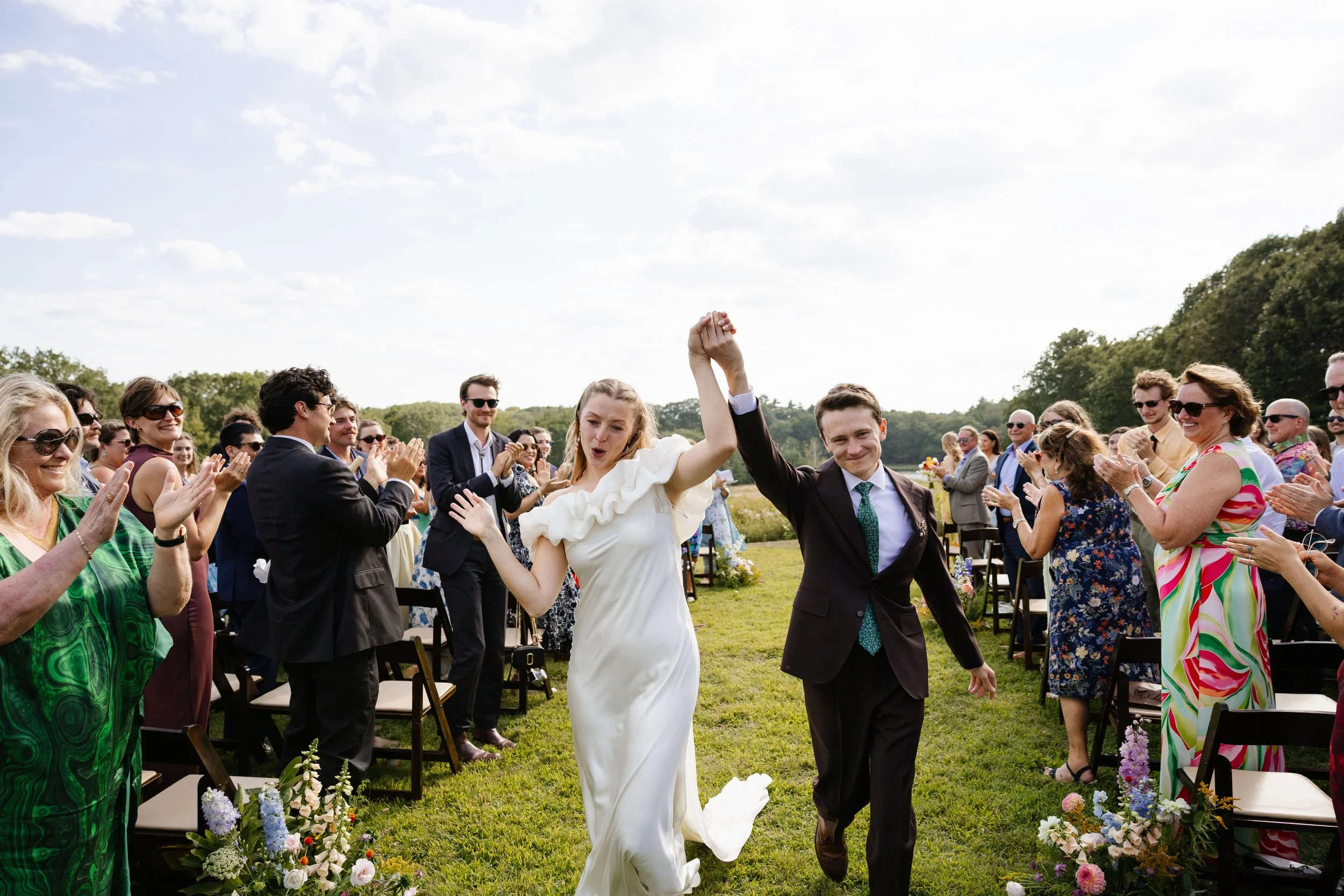 A couple and their guests together during a ceremony in the field at Scotland Fields in York, Maine. Photography by Sienna Renee Photography.