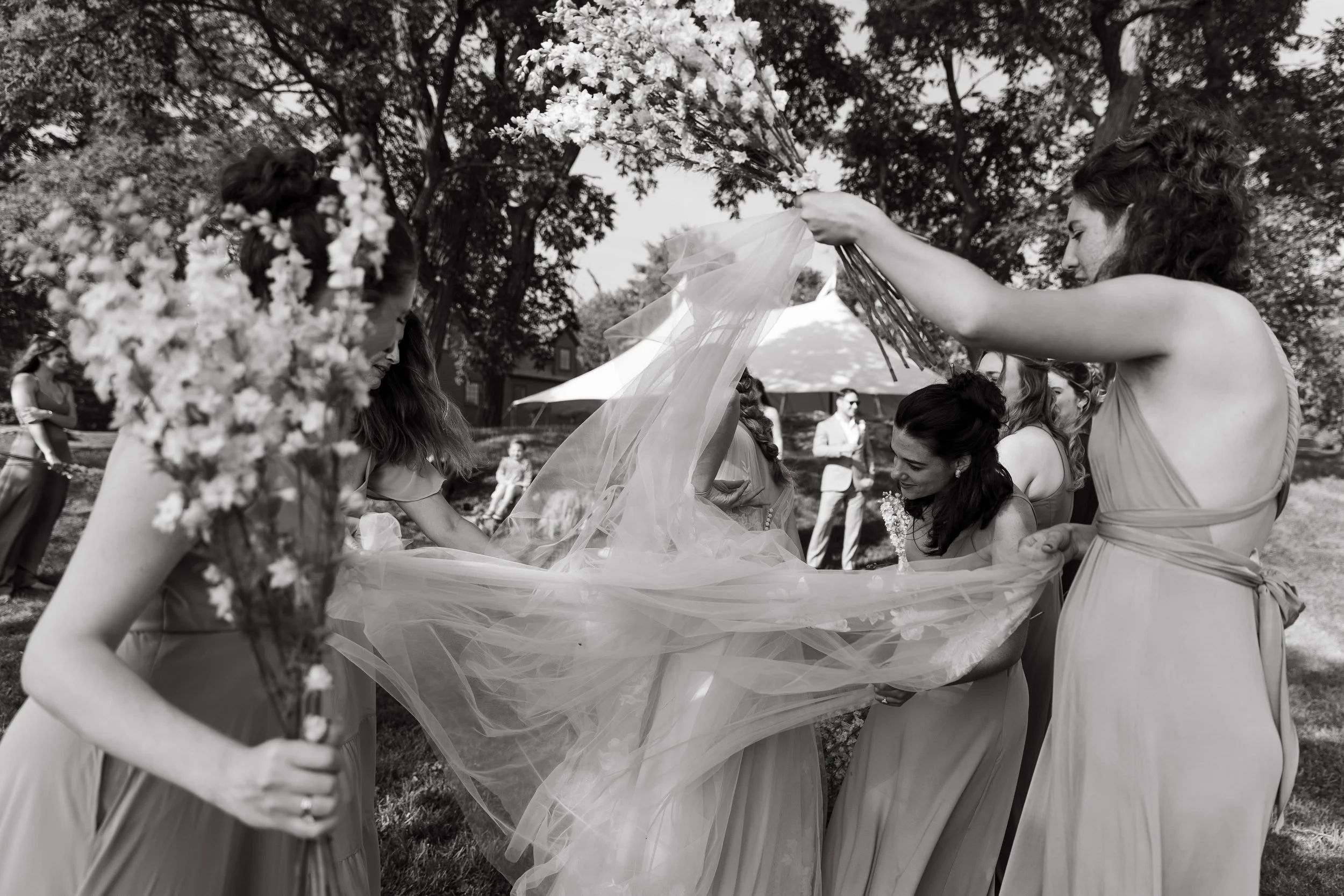 A bride surrounded by friends as they help her with her dress during her small wedding day in Kittery, Maine. Photography by Sienna Renee Photography.