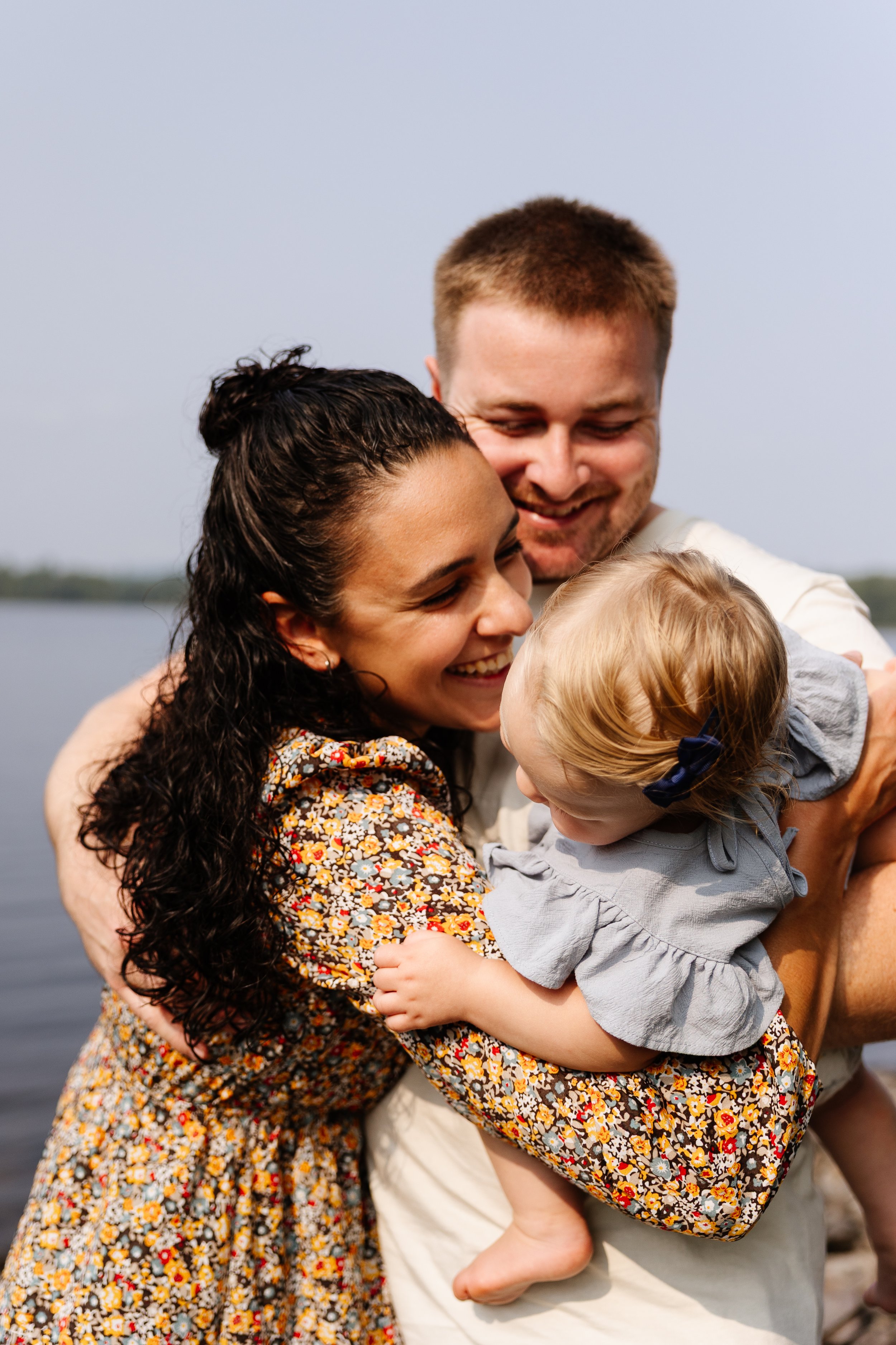 A young family hugs and smiles during a walk around their rental in Rockwood, Maine. Photography by Sienna Renee Photography.