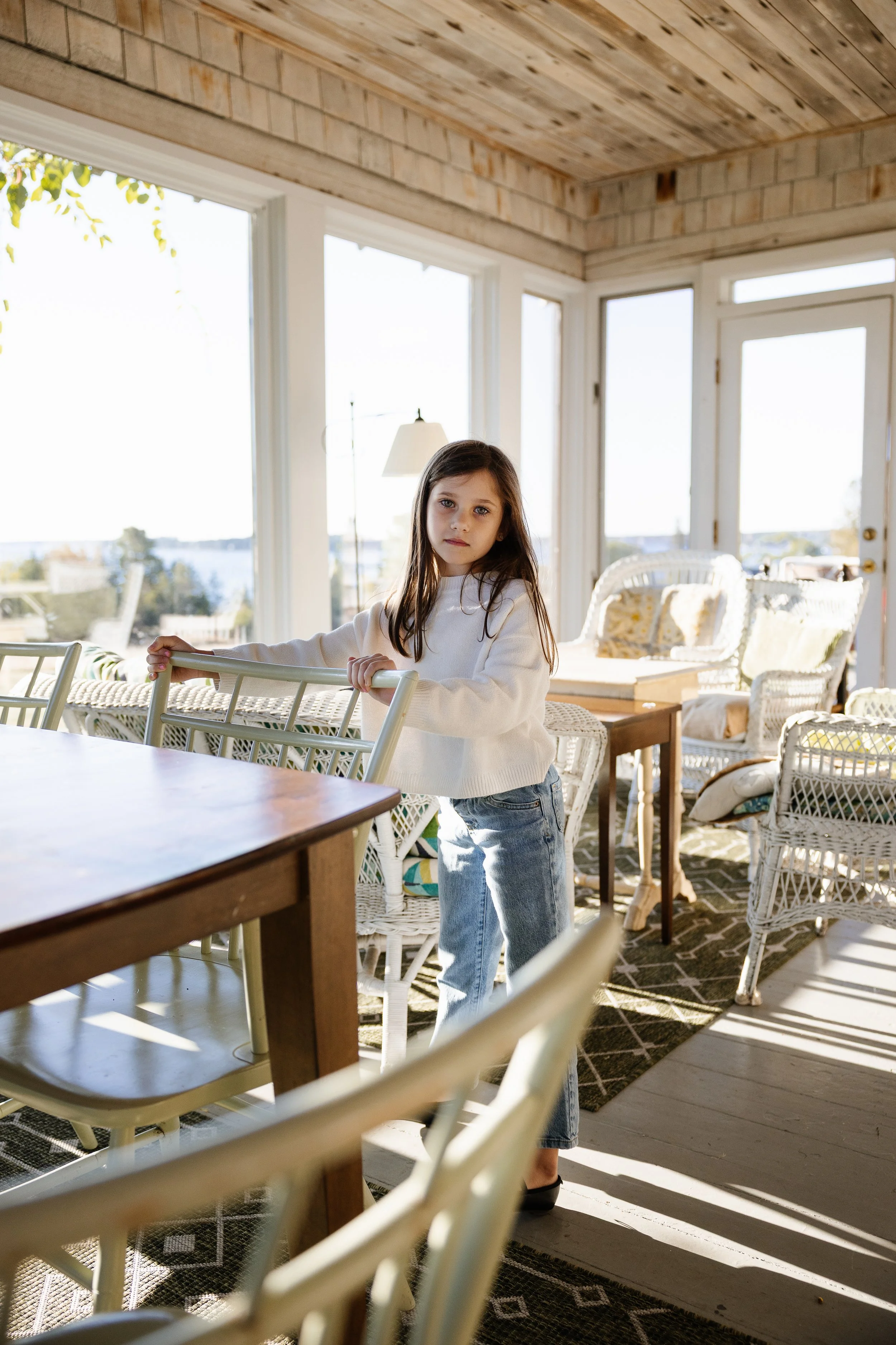 A girl looks at the camera with curiosity during an at home photography session during a visit with family to Southwest Harbor, Maine. Photography by Sienna Renee Photography.