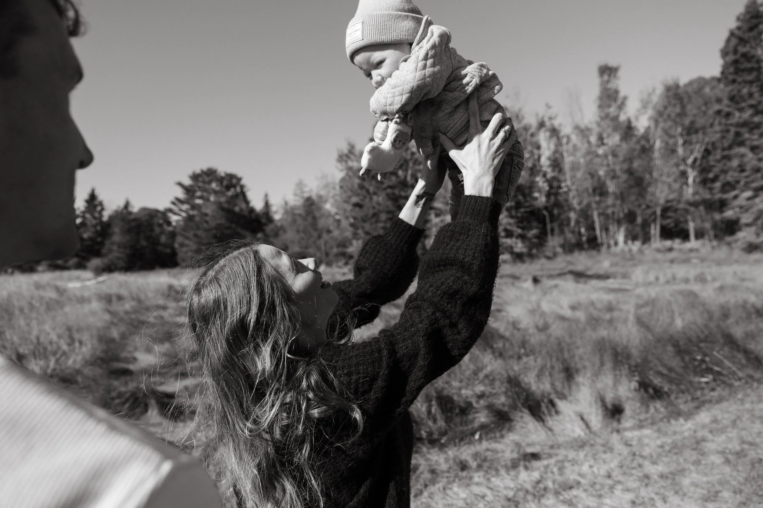 A mom holds her baby up while her partner looks at the two of them. Photography by Sienna Renee Photography.