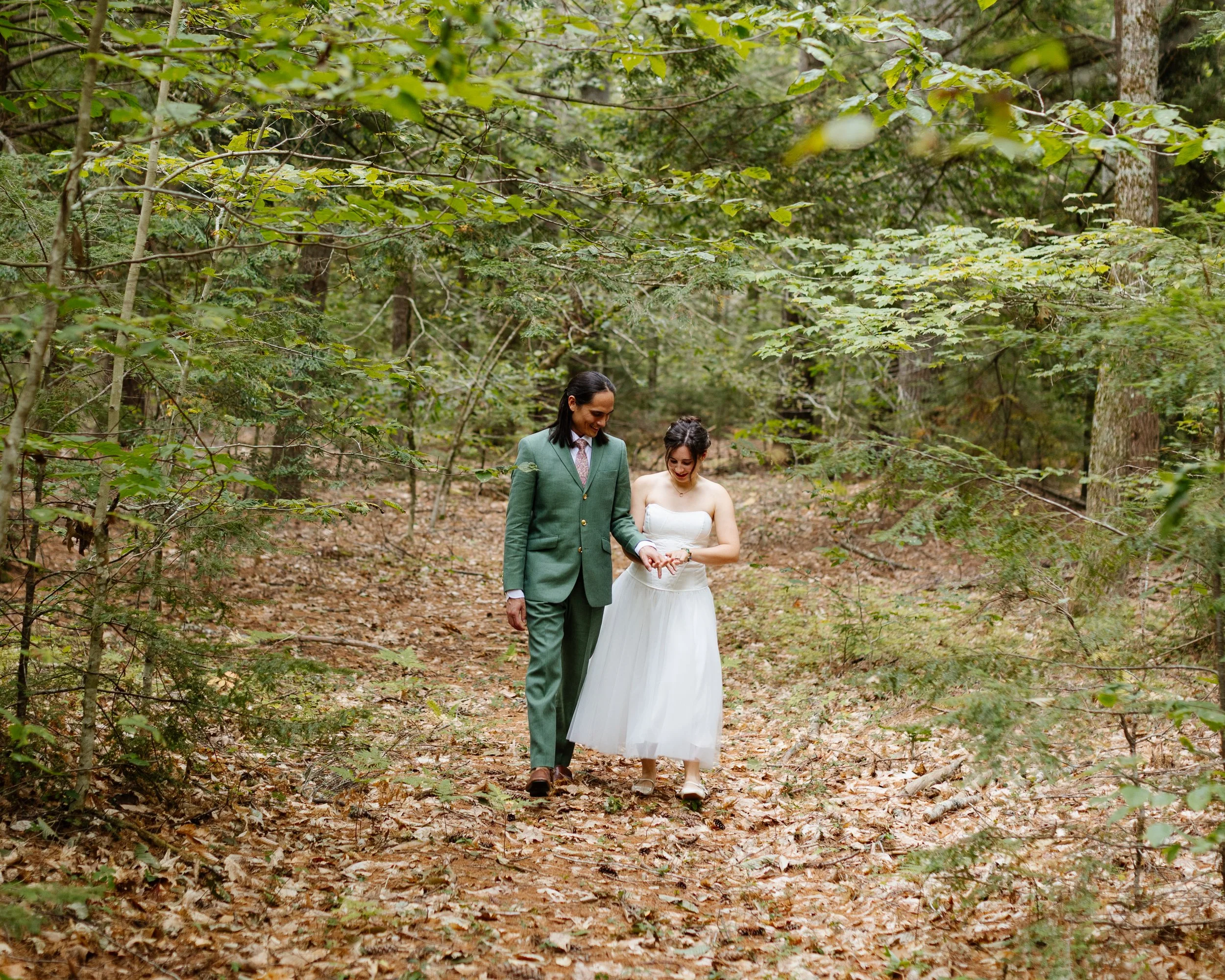 A couple walks in the woods on a family property during their backyard wedding in Maine. Photography by Sienna Renee Photography.