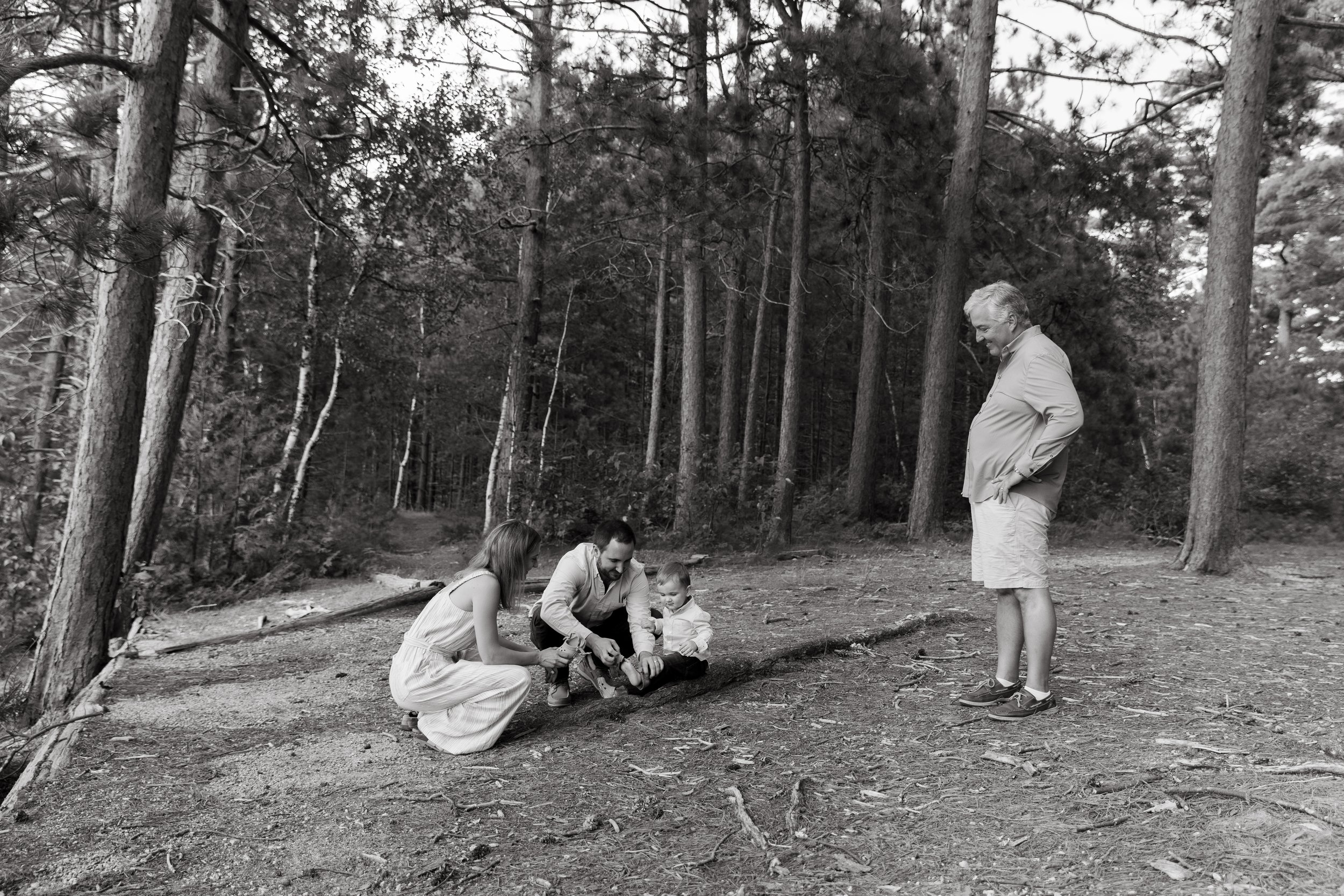 A couple puts on their toddler's shoes during a walk in the woods with grandparents in Baxter State Park, Maine. Photography by Sienna Renee Photography.