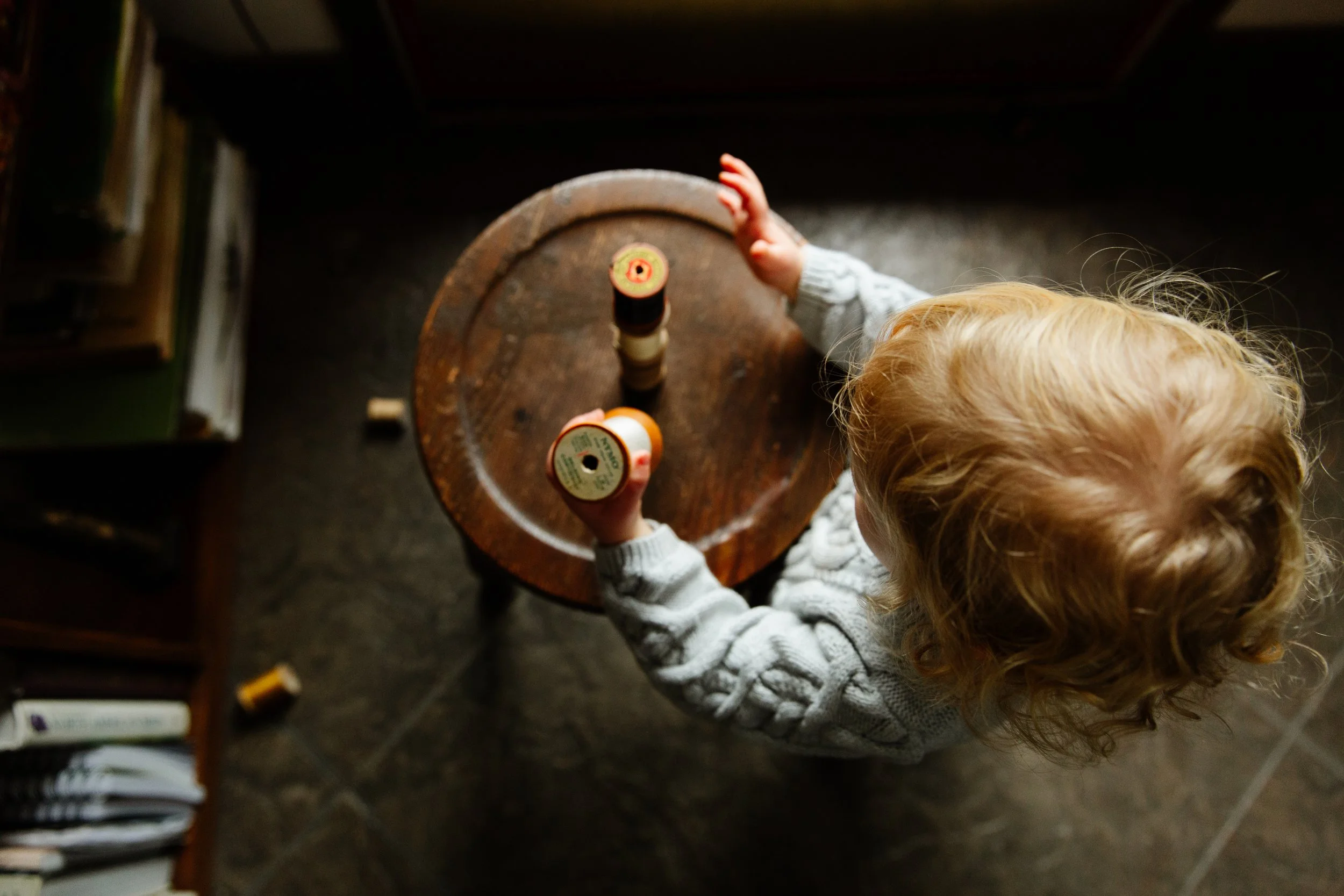 A toddler plays with spools at her grandmother's house during an at home photography session. Photography by Sienna Renee Photography. 