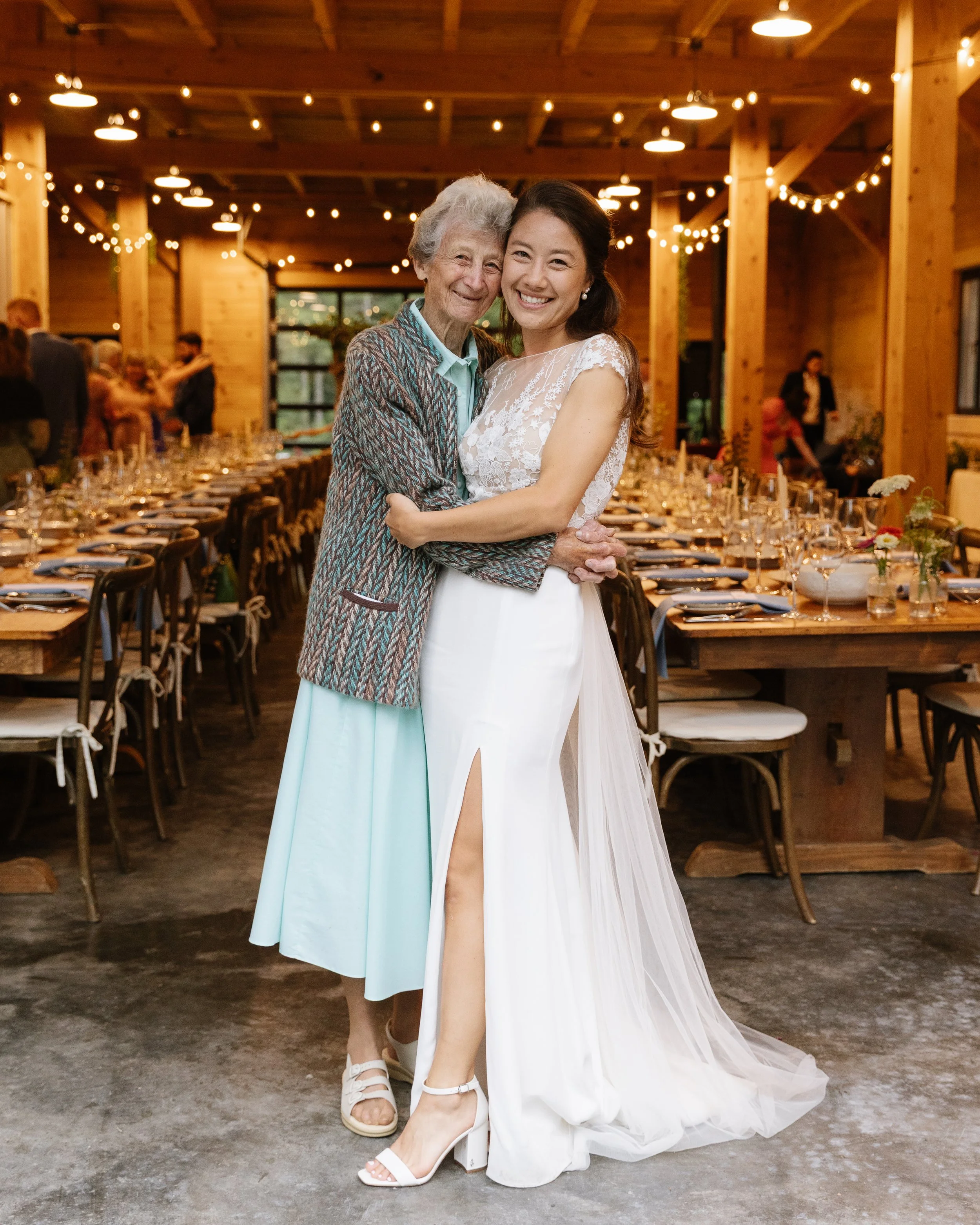 A bride hugs her grandma while they smile towards the camera during her backyard wedding in Dover-Foxcroft, Maine. Photography by Sienna Renee Photography.
