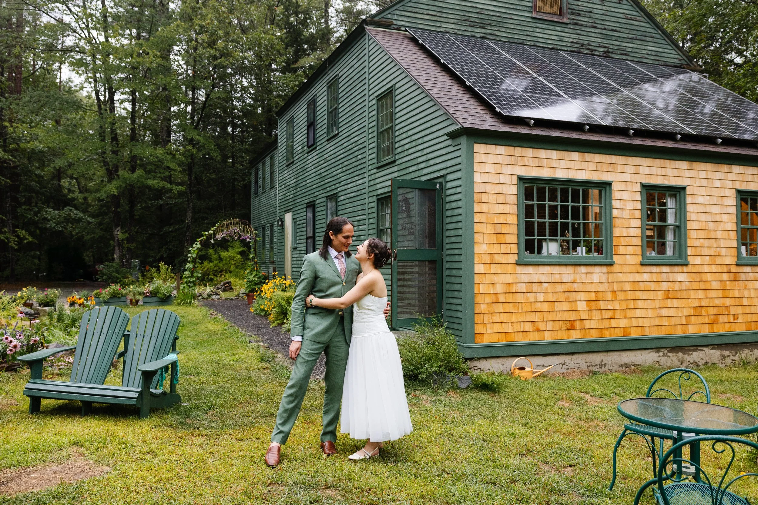 A couple stands in front of a family home during their backyard wedding day in Maine. Photography by Sienna Renee Photography.