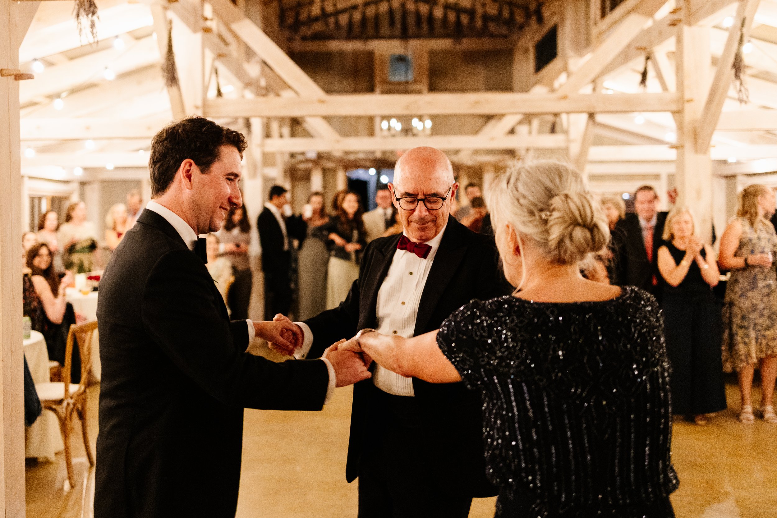 A groom and his parents dance together during his wedding day at Marianmade Farm in Wiscasset, Maine. Photography by Sienna Renee Photography.