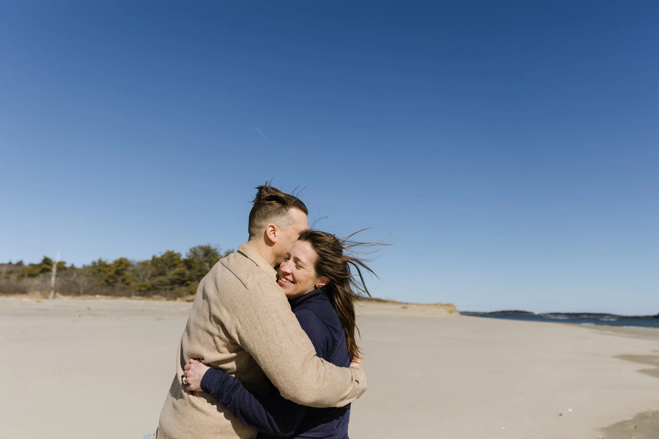 A couple holds each other and miles during a walk at Popham Beach in Phippsburg, Maine. Photography by Sienna Renee Photography.