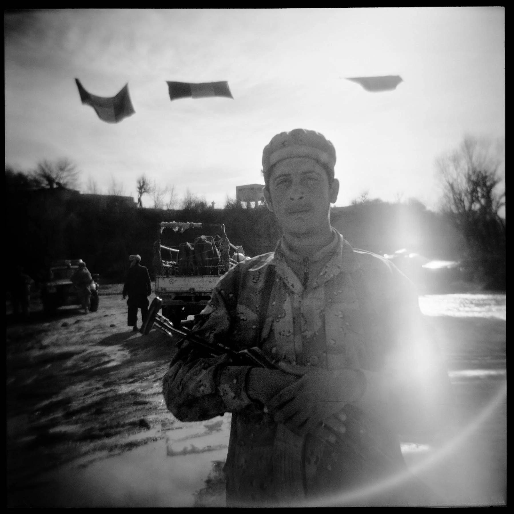 A young Afghan Border Police officer mans a border crossing post under the watchful eyes of American soldiers in FOB Tillman (background). Gayan district, Paktika province, 2011.