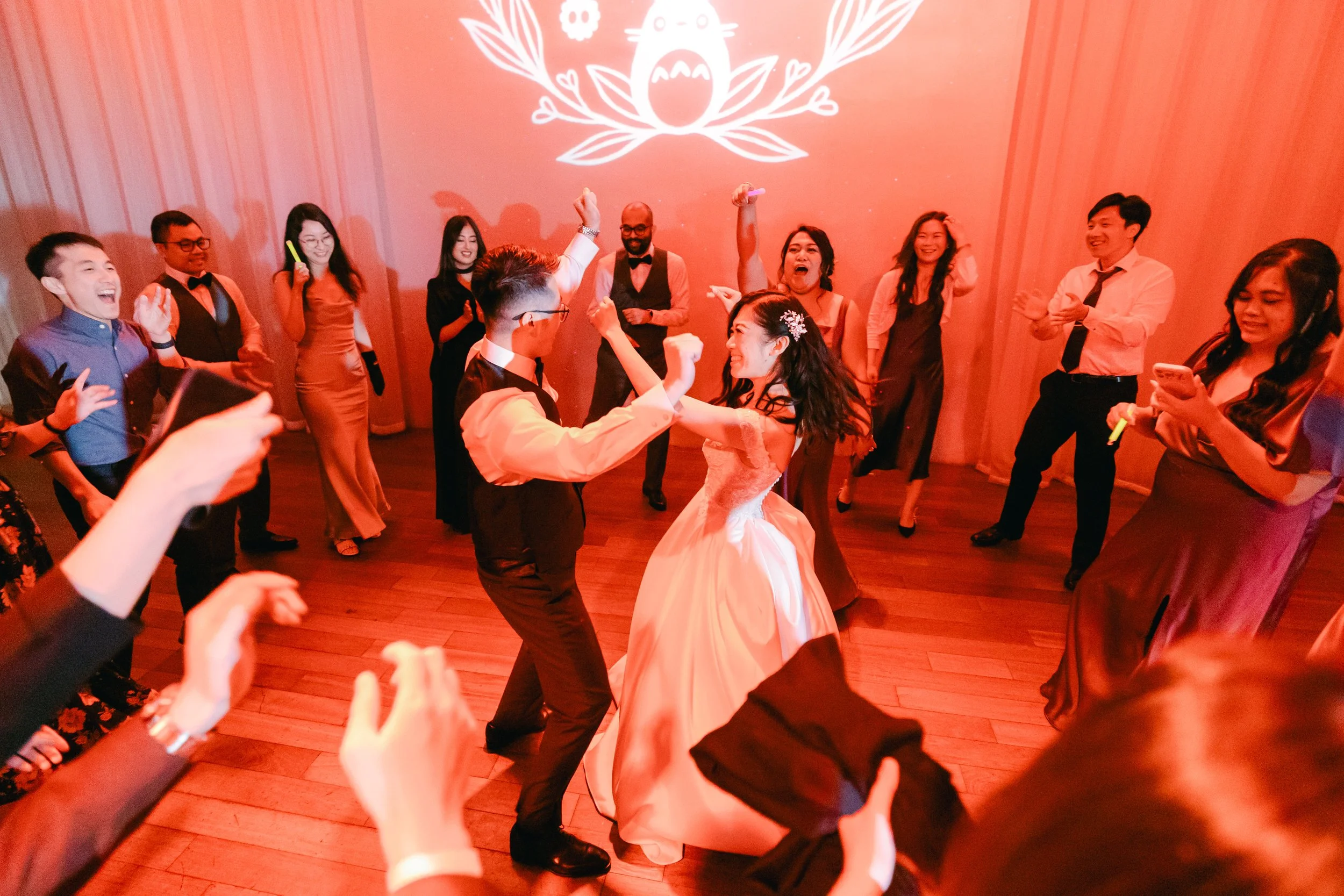 A bride and groom dancing joyfully at their wedding reception, surrounded by guests who are celebrating and dancing.