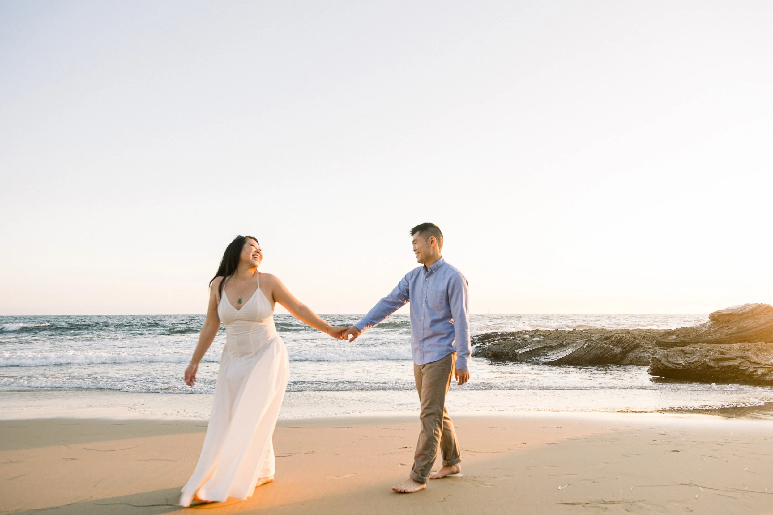 A couple holding hands and dancing on the beach during sunset.