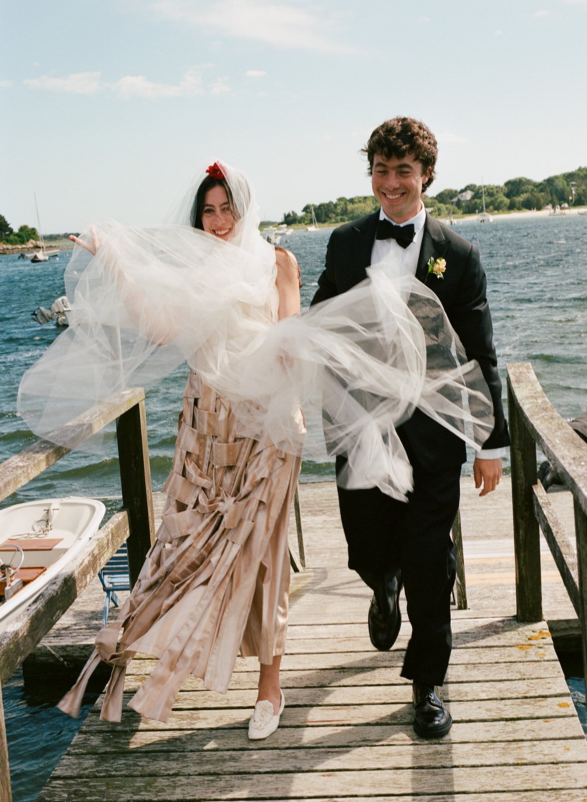 Artful couple walks along dock after cape cod wedding ceremony in Falmouth, Massachusetts.