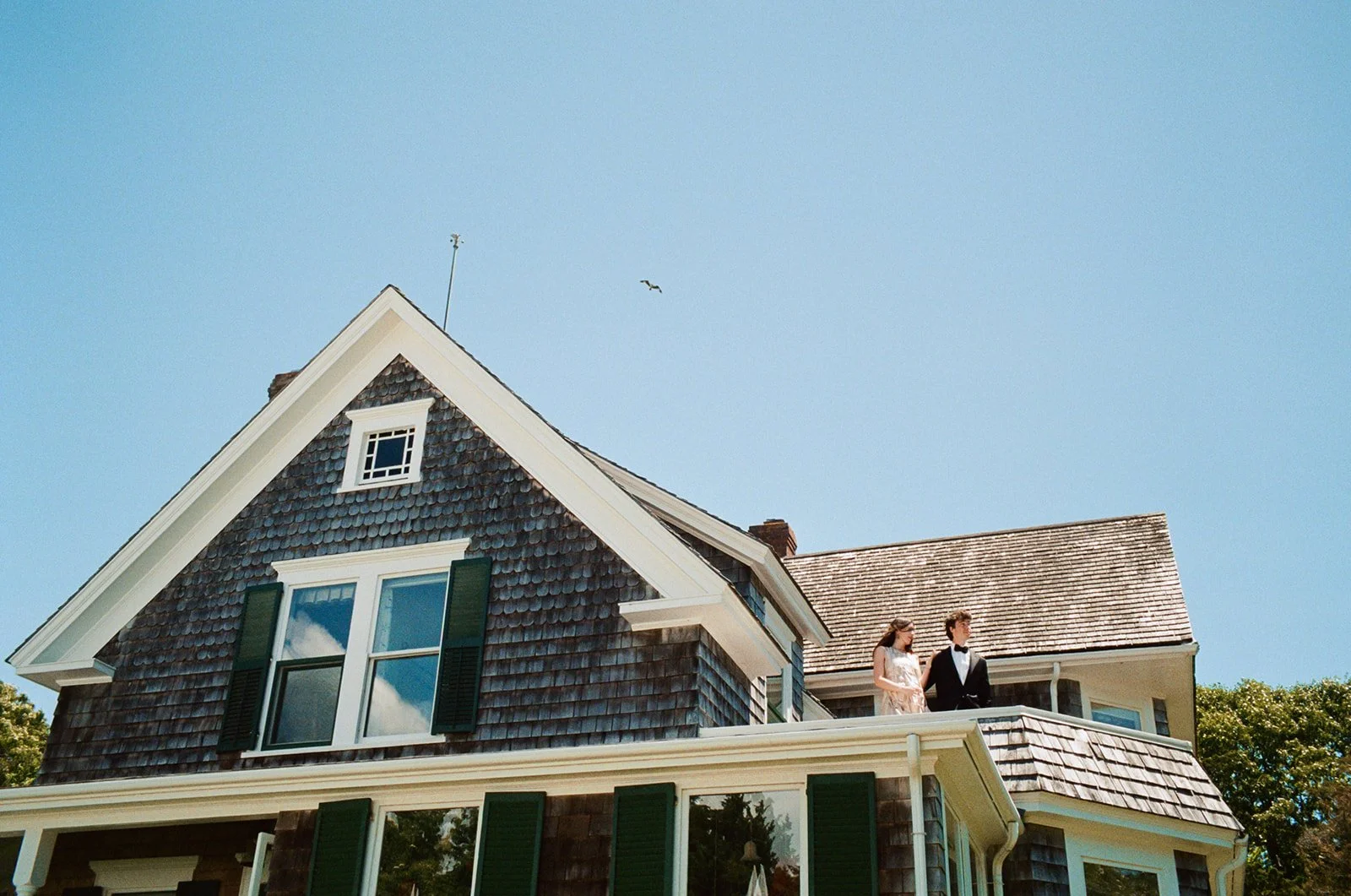 A bride and groom stand for a film portrait atop a roof of a family home on Cape Cod, Massachusetts