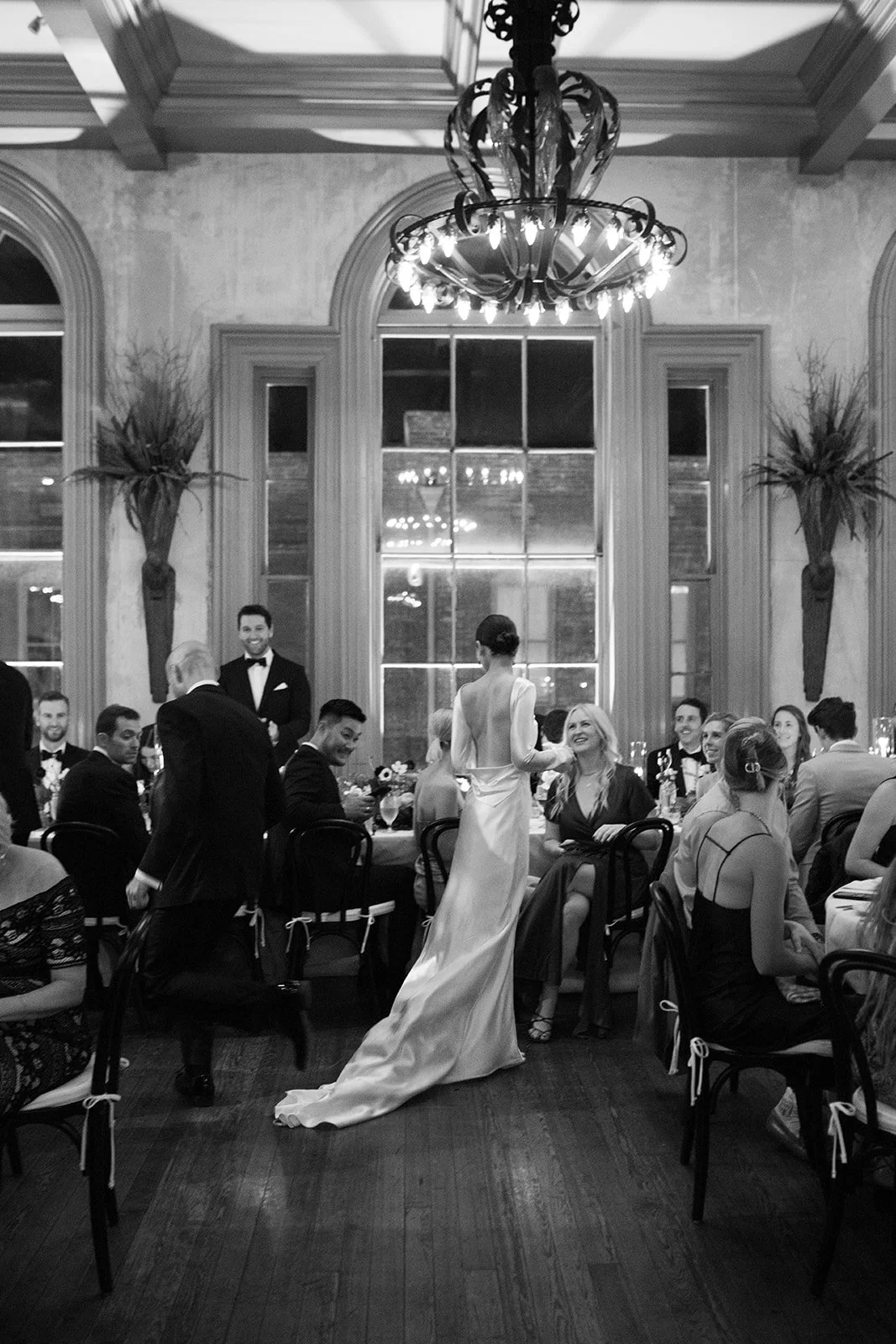 An elegant bride stands and talks to guests in her draping Danielle Frankel gown during her ball room wedding reception in Savannah Georgia.