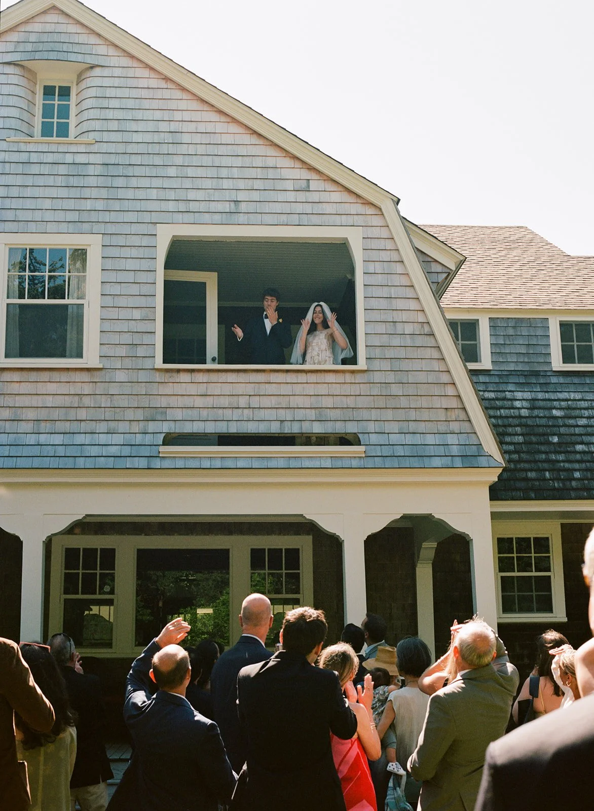 Couple waves to wedding guests from deck of Cape Cod house in Massachusetts.