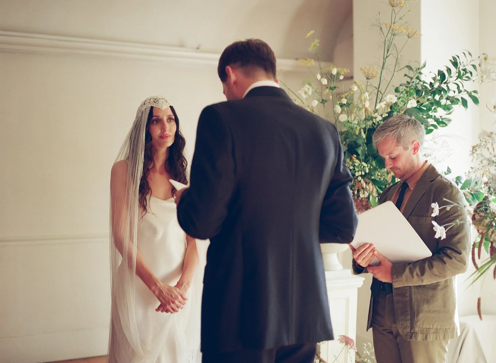 Bride in custom Paula Nadal listens as groom gives speech during wedding ceremony at Stissing House in Upstate New York.