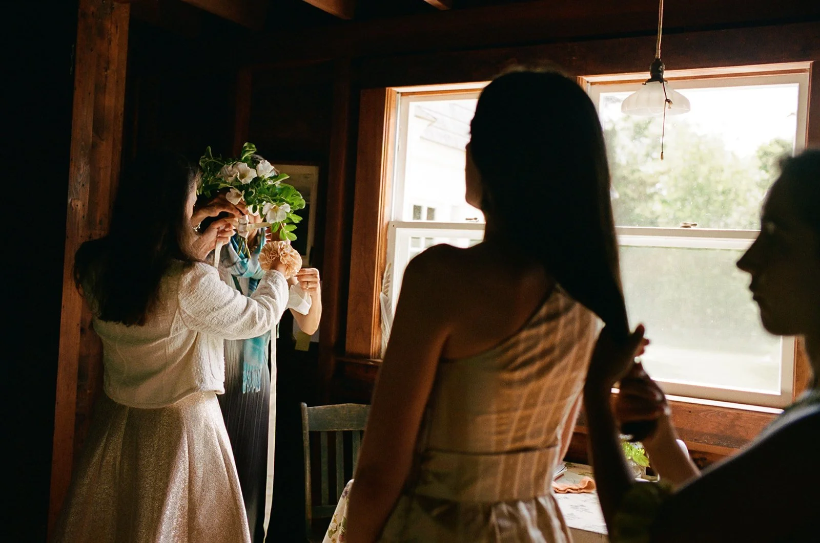 A bride's family wraps ribbon around her floral bouquet just before her wedding ceremony in the woods of Falmouth Cape Cod, Massachusetts.