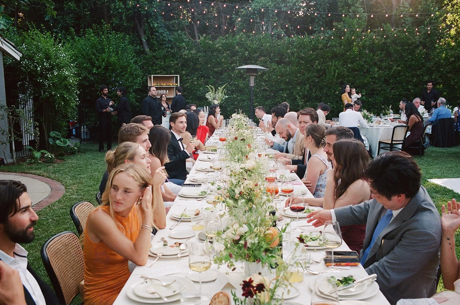 Wedding guests sit for family-style dinner at outdoor reception in Pasadena, California.
