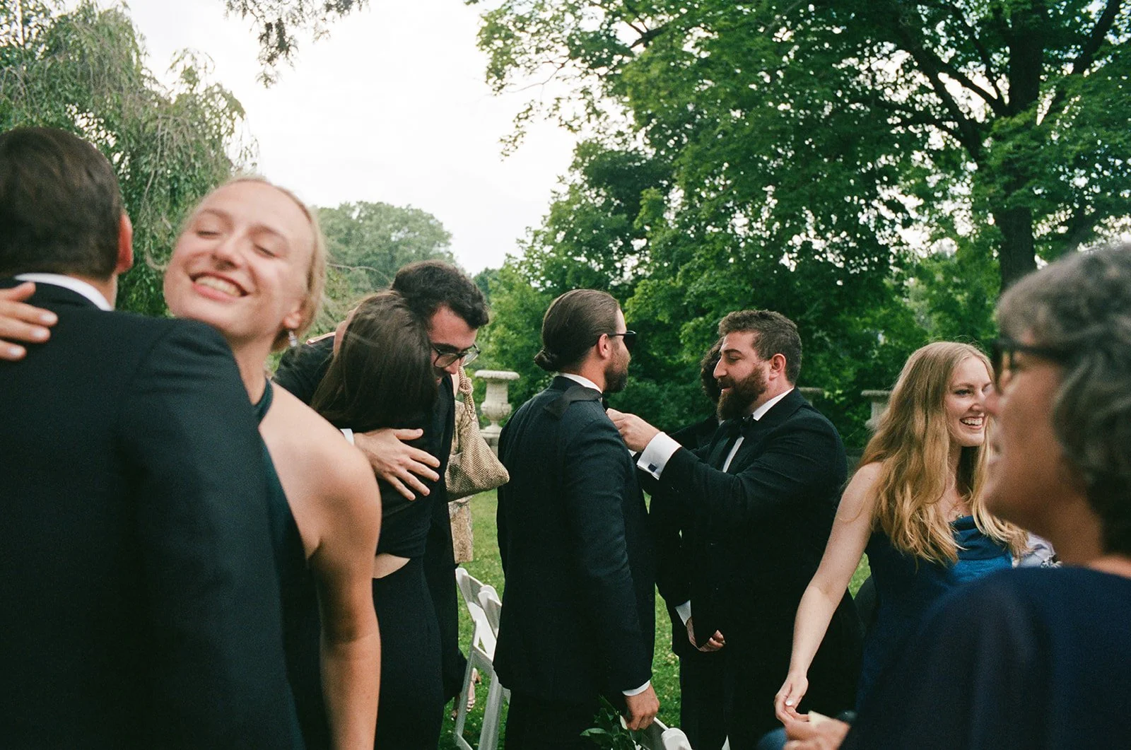 Wedding guests smile and hug before ceremony at Cranbrook House and Gardens outside of Detroit, Michigan.