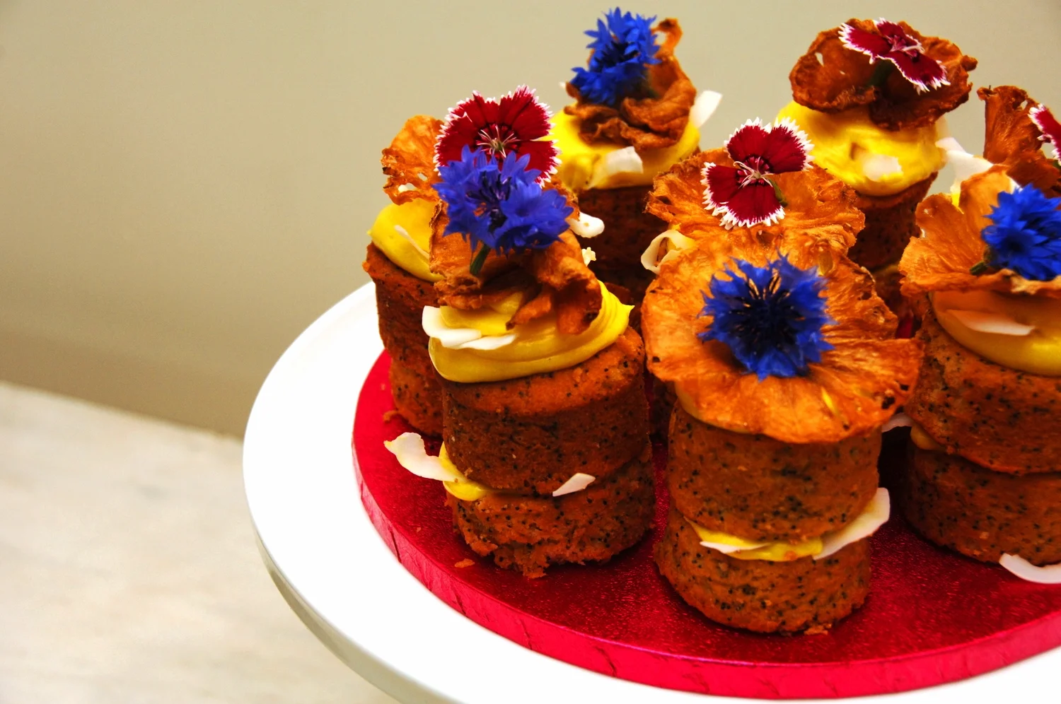   Lemon, Coconut and Pineapple Cakes    Moist zesty lemon and poppy seed mini layer cakes with homemade lemoncurd, a smooth lemon buttercream, coconut shards edible flowers and pineapple petals. 