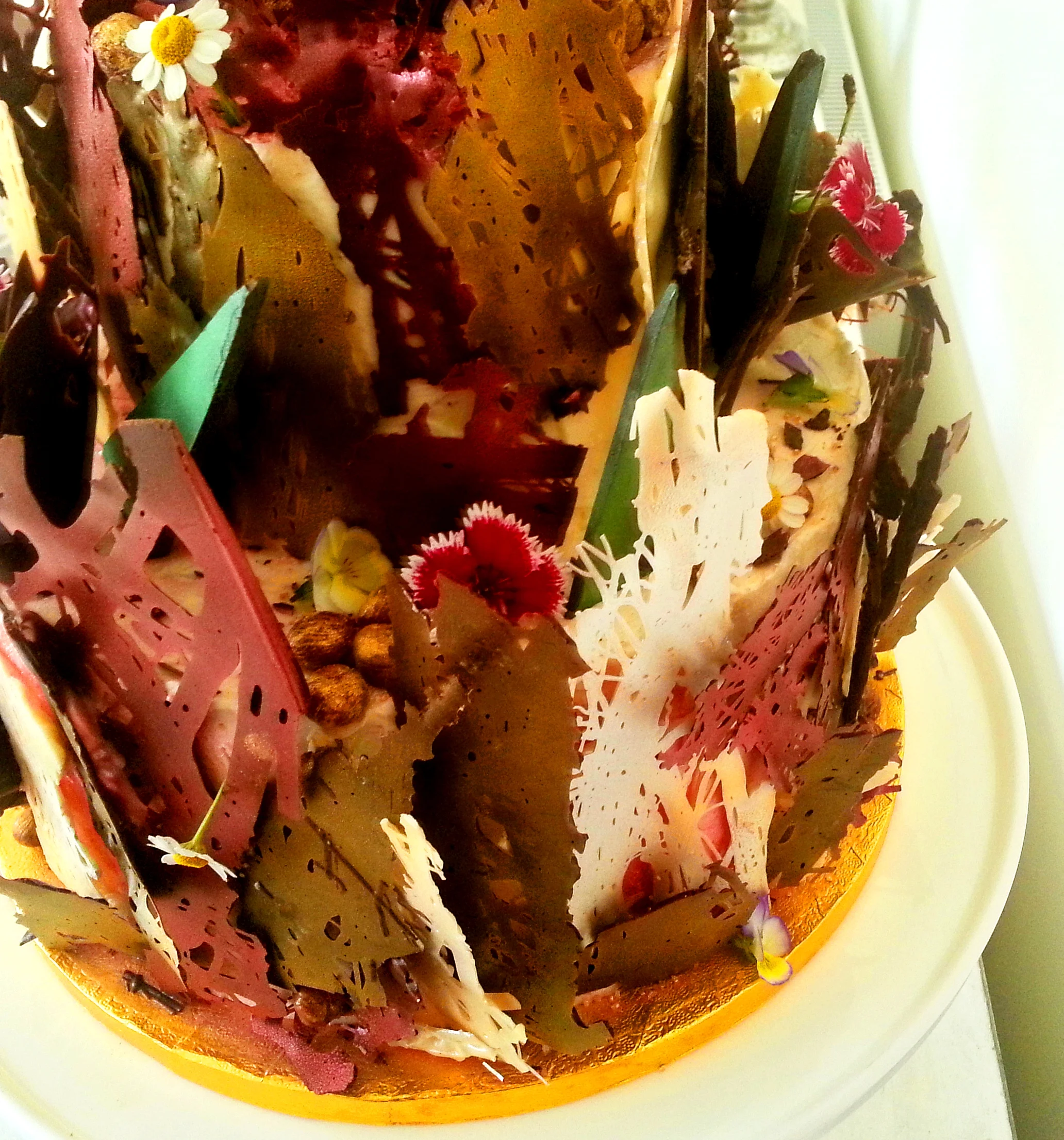 Lace chocolate tapestry with metallic green chocolate leaves and edible flowers.