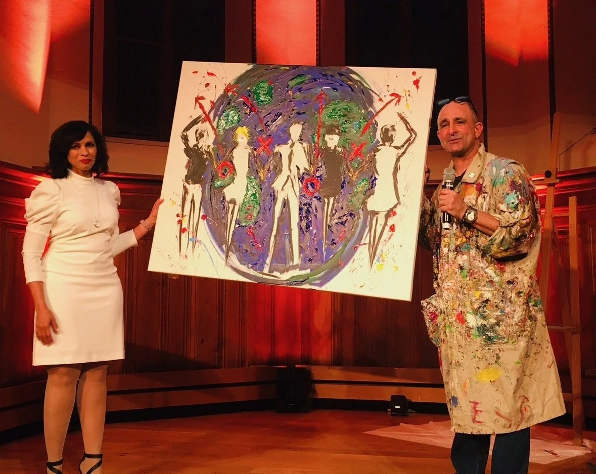Jeff Sparr and Seema Kumar stand on stage holding a colorful abstract painting of five figures in front of a large globe.