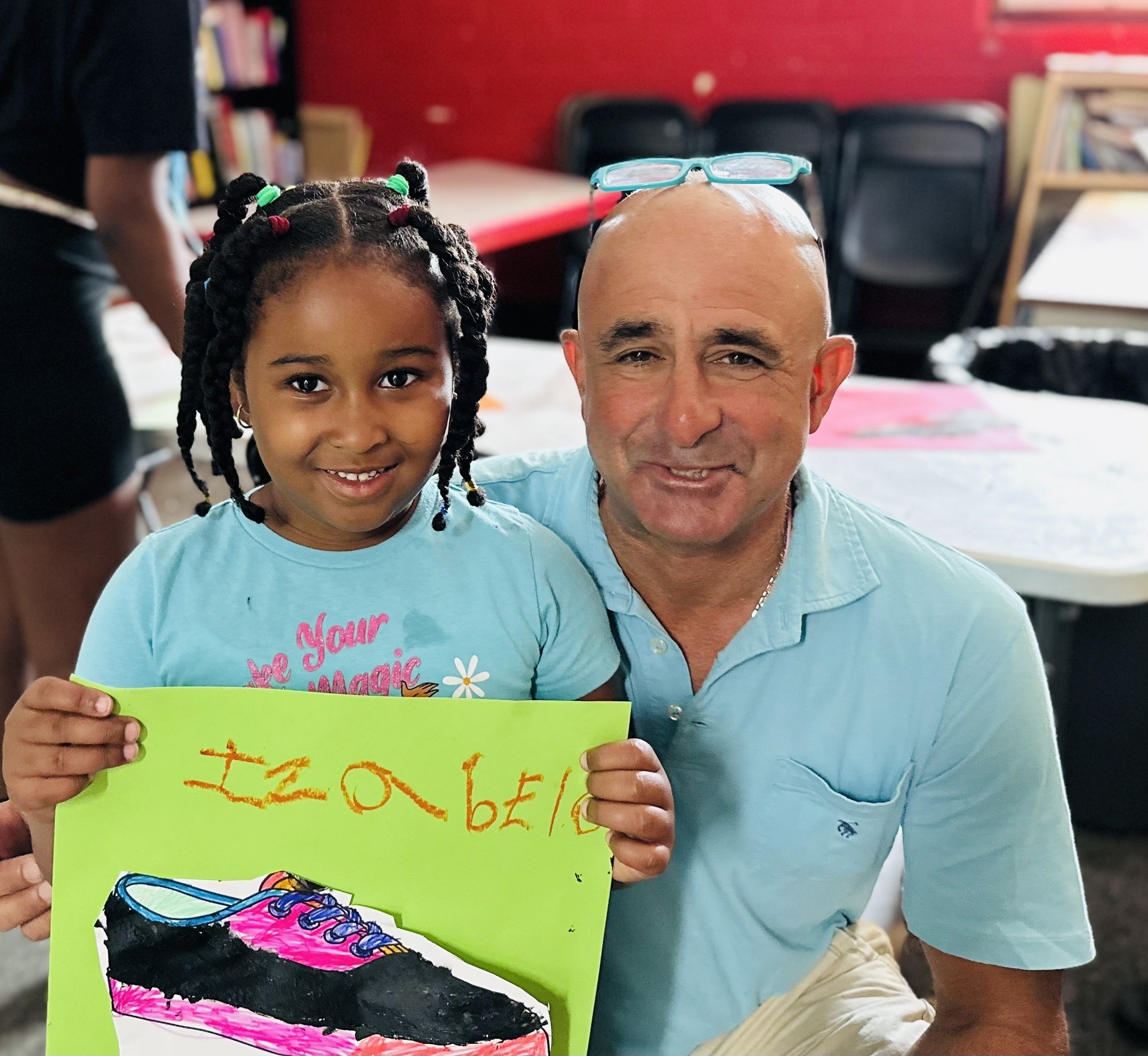 Jeff and a girl smiling while she holds up her drawing of a shoe