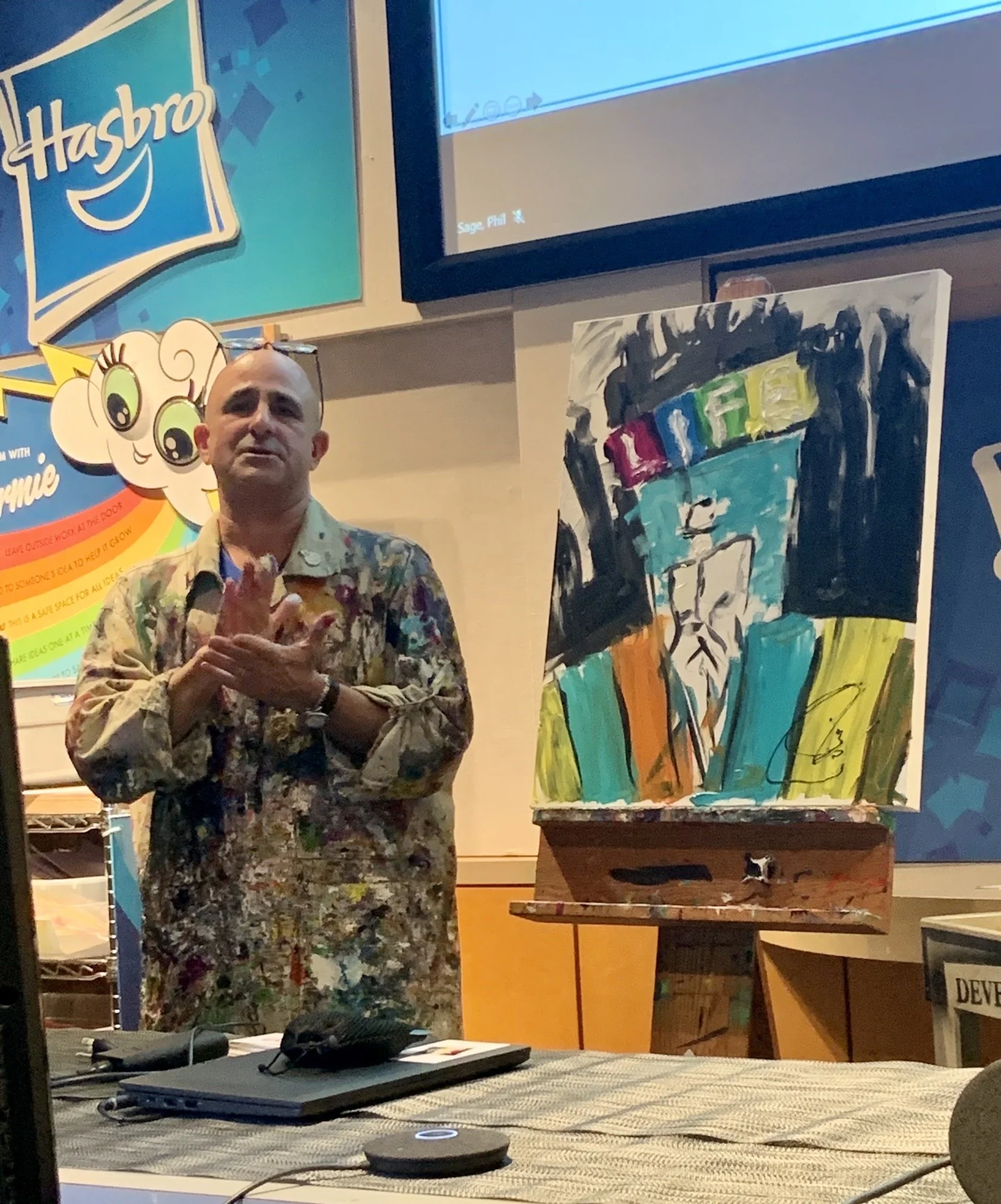 Jeff speaking at Hasbro, standing next to a painting that alludes to "The Game of Life"