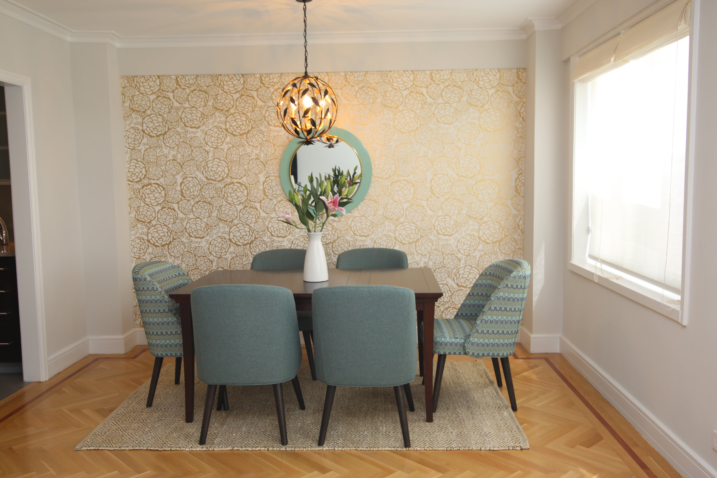 Dining room with different color chairs, gold floral chandelier and jute rug 