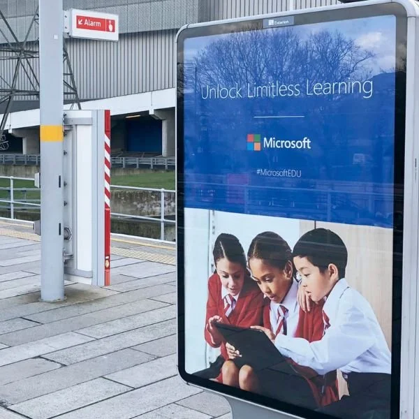 Billboard advertisement for Microsoft featuring three children in school uniforms looking at a tablet, with the text 'Unlock Limitless Learning' and the hashtag #MicrosoftEDU.
