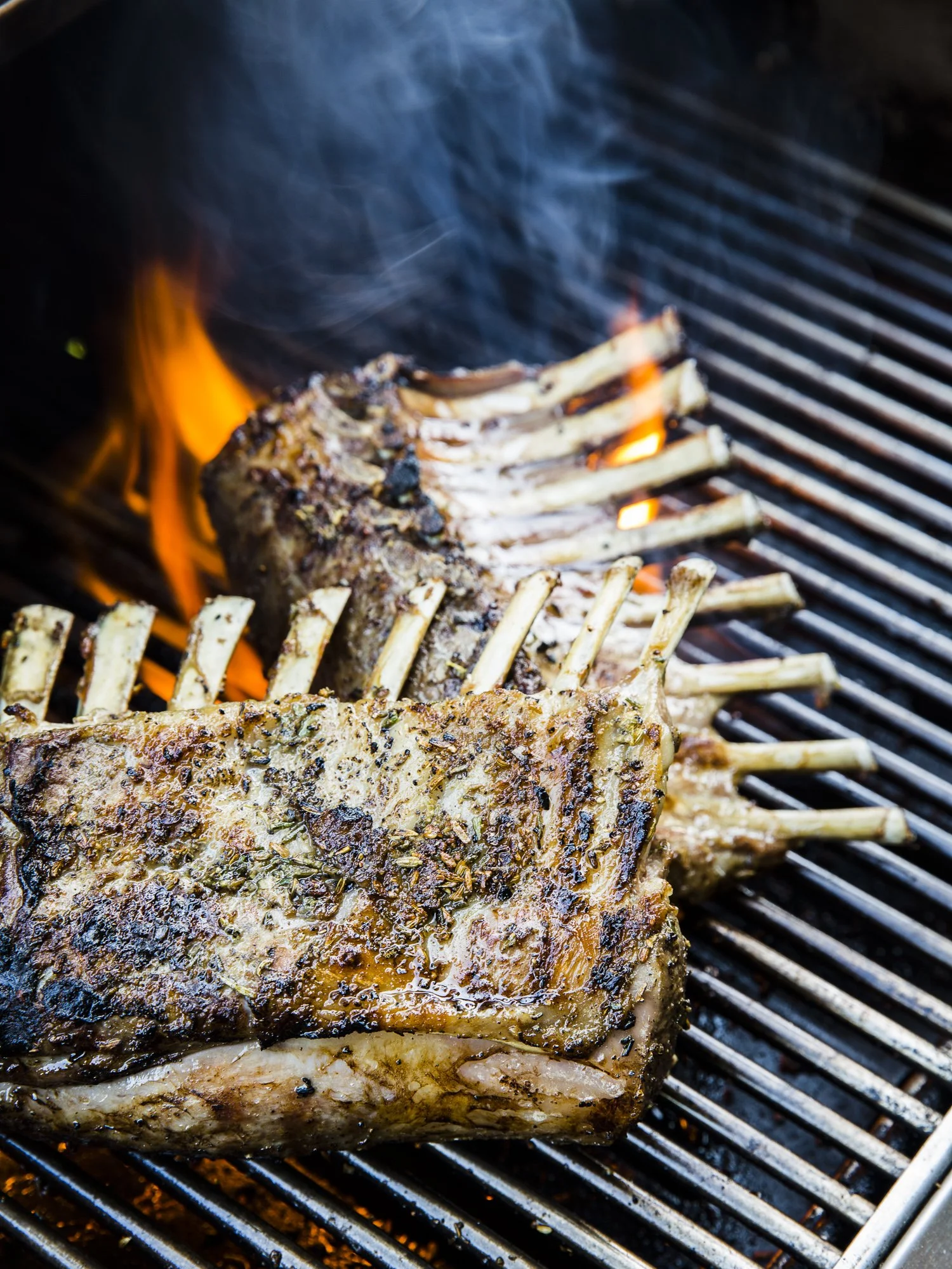 Lamb chops grilling on a barbecue with flames and smoke in the background.