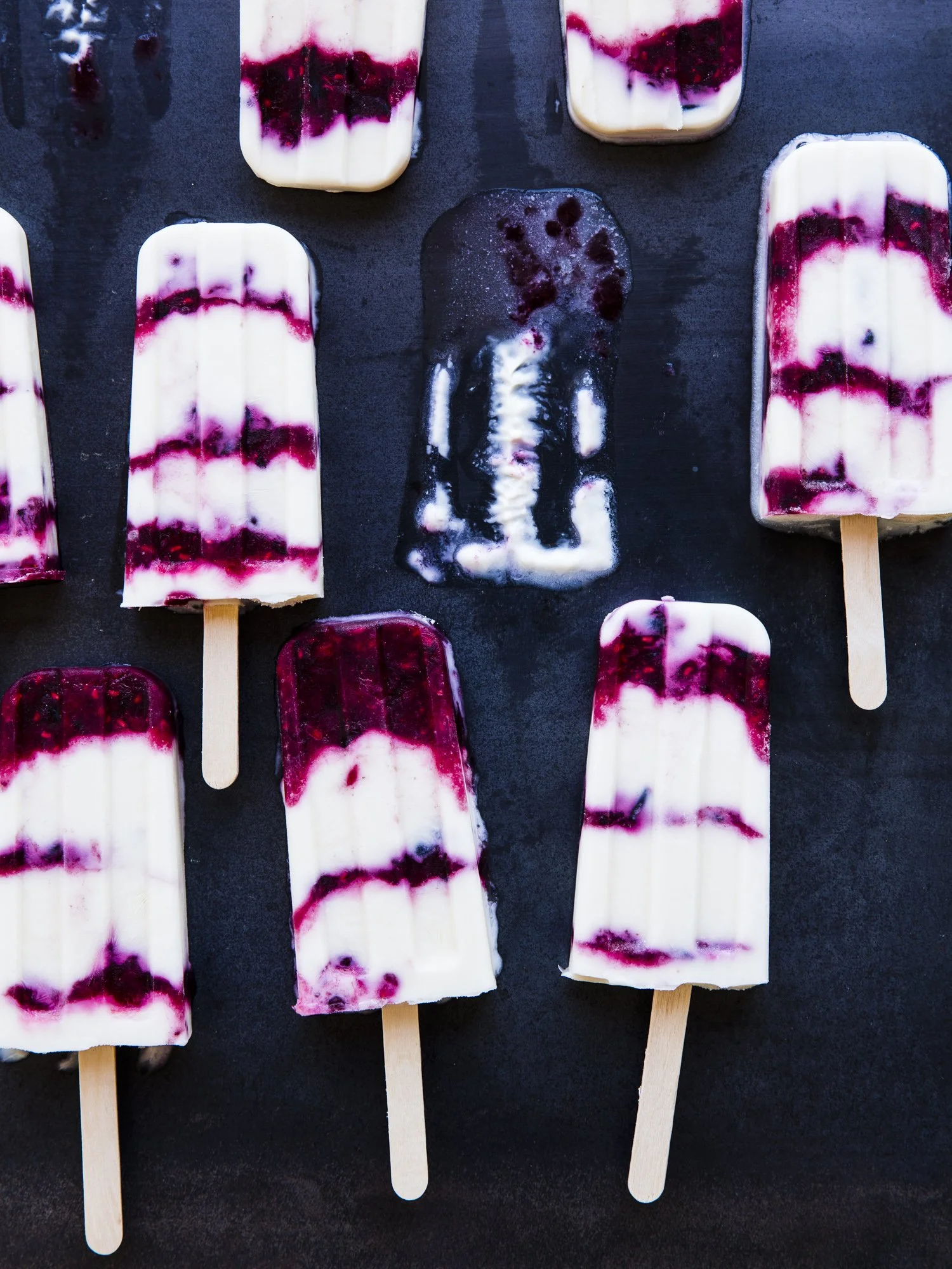 A group of berry-flavored popsicles with a white and dark red swirled pattern on a black surface.