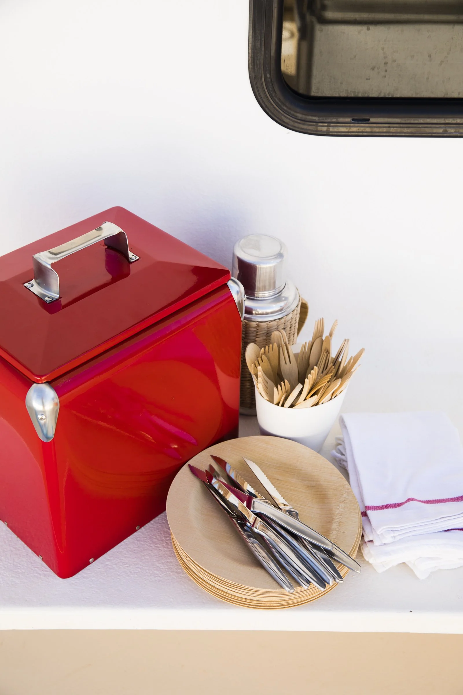 A red napkin dispenser, a small container with utensils, and a stack of white napkins on a white surface.