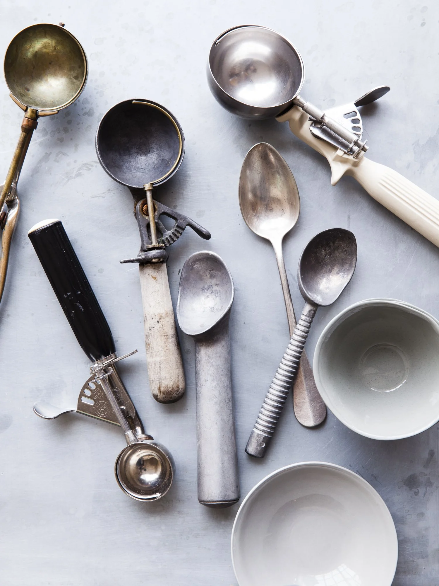 Collection of vintage and modern ice cream scoops and bowls on a light gray surface.