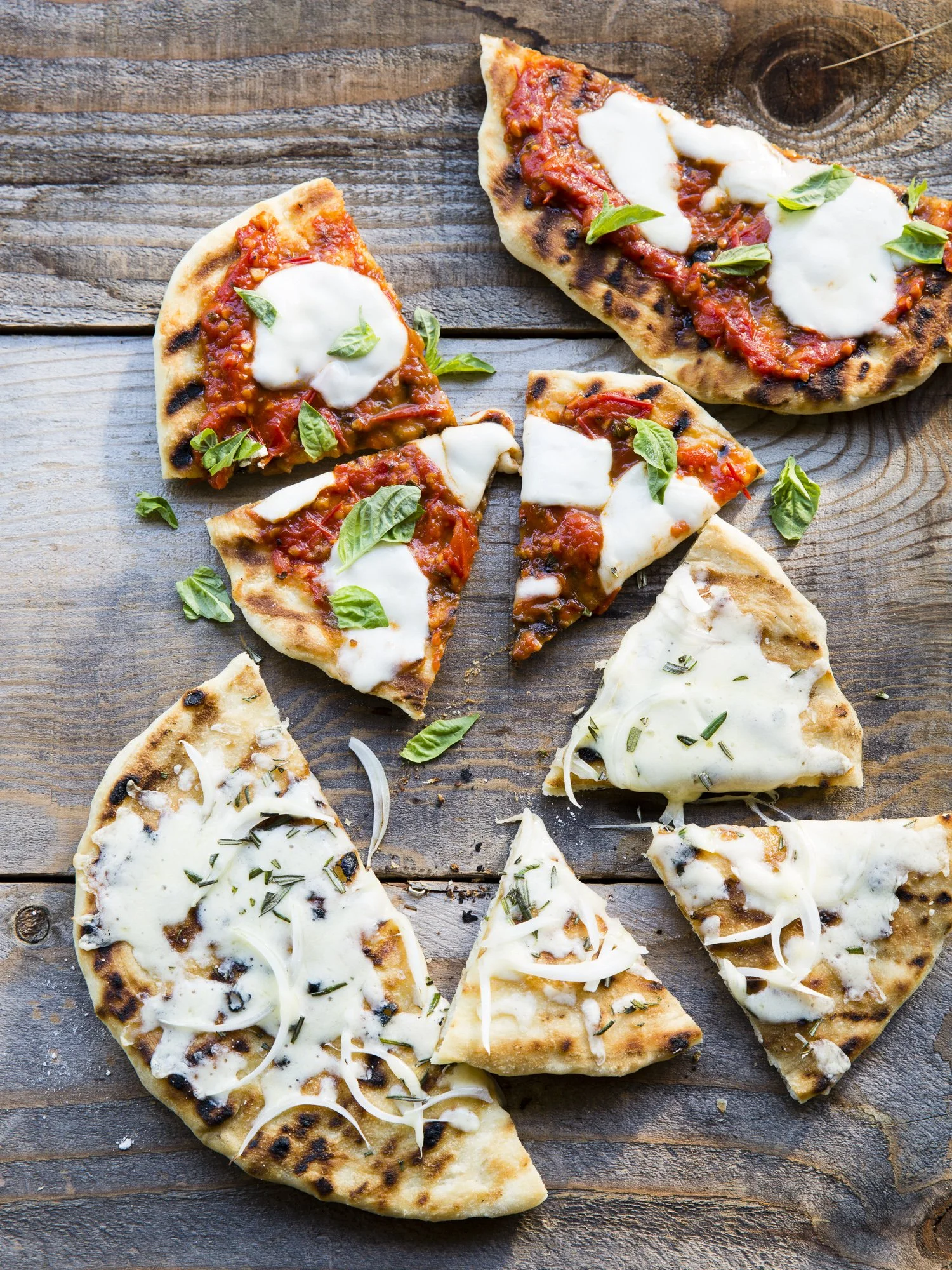 Several slices of pizza with different toppings, including cheese, tomato sauce, basil, and herbs, on a rustic wooden surface.
