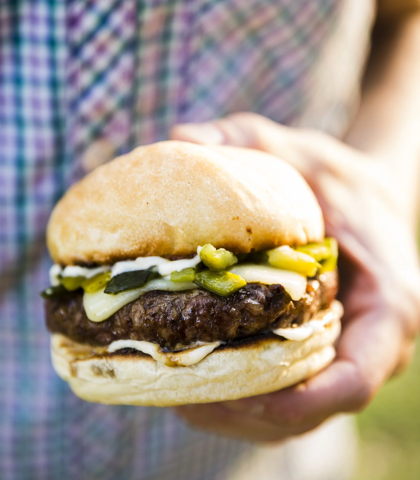 Close-up of a person holding a cheeseburger with pickles, onions, and mayonnaise in a bun.