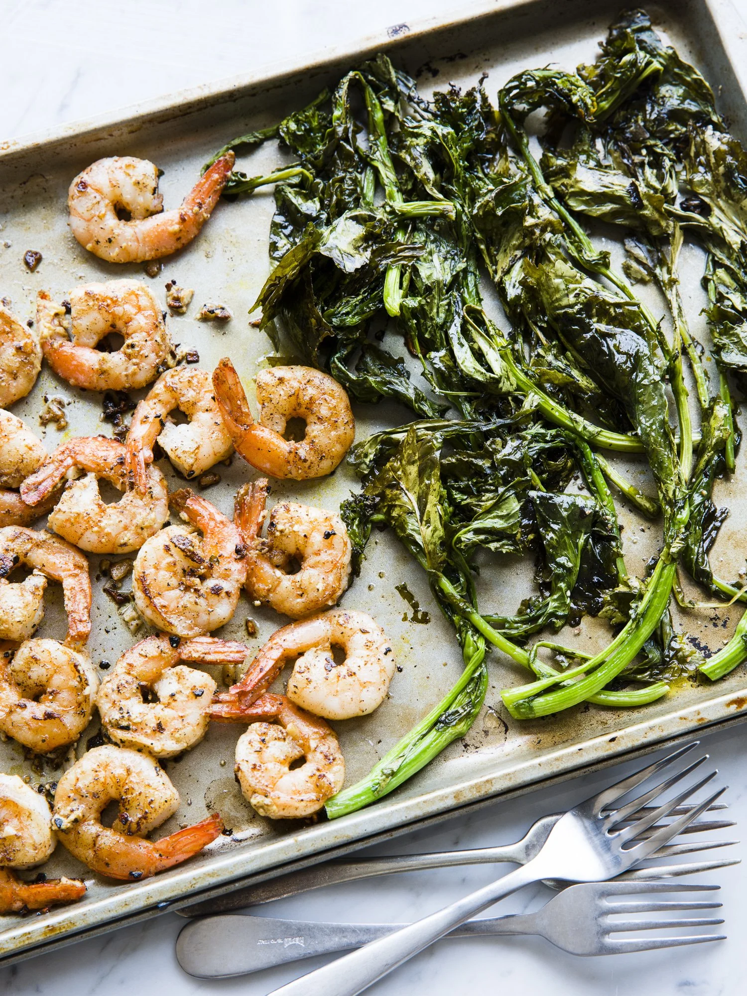 Cooked shrimp and sautéed greens on a baking sheet